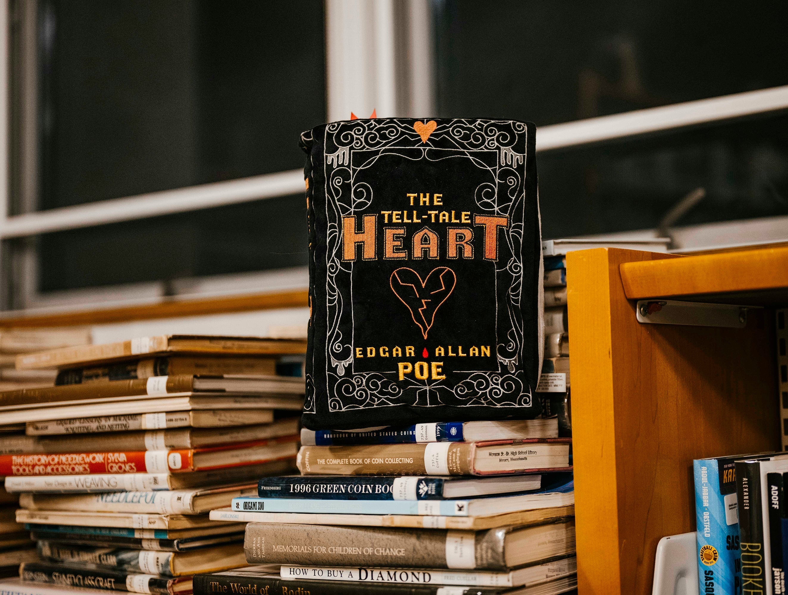 A book plushie of the tell-tale heart sitting on a stack of books in the library
