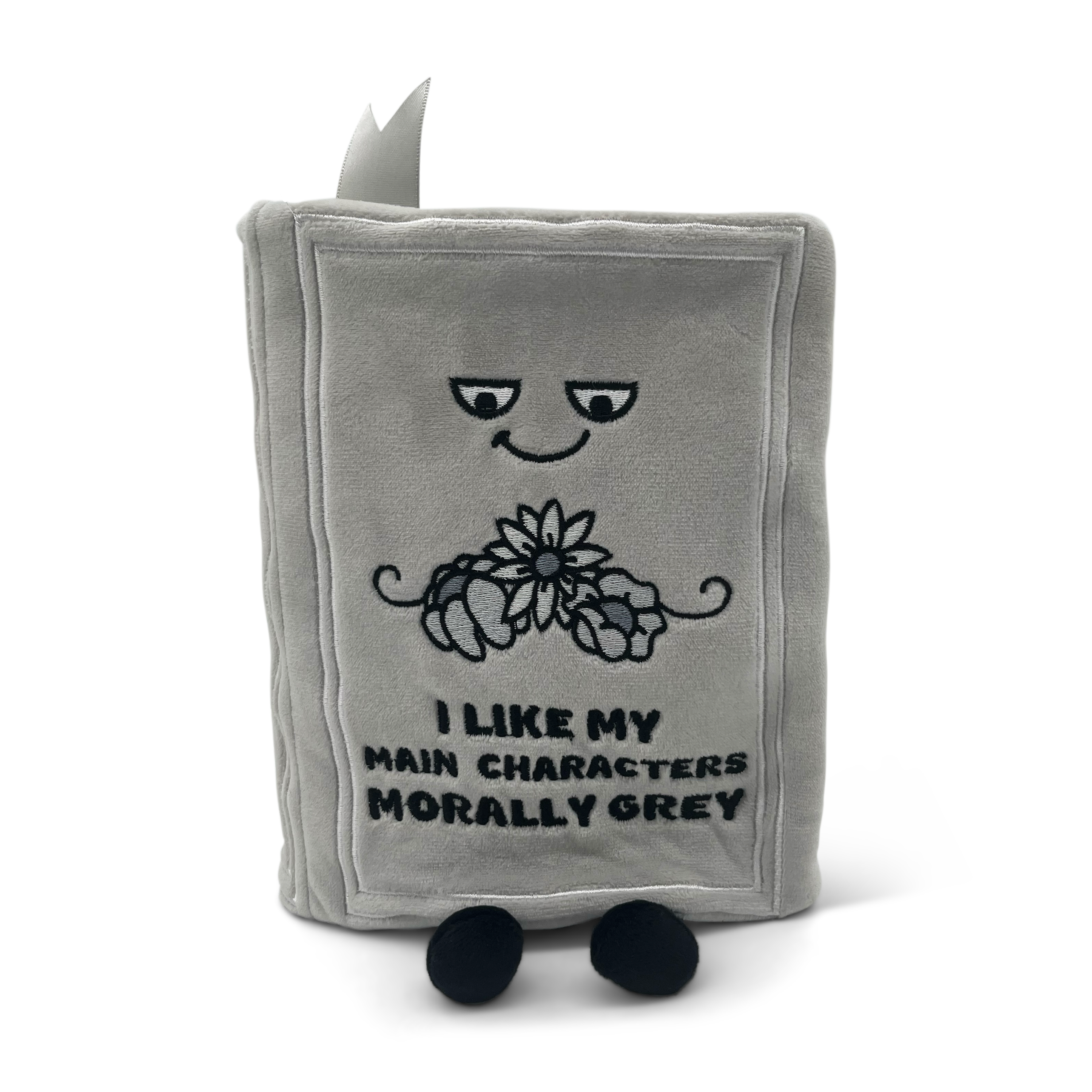 A gray plush book with the text 'I LIKE MY MAIN CHARACTERS MORALLY GREY' on the cover.