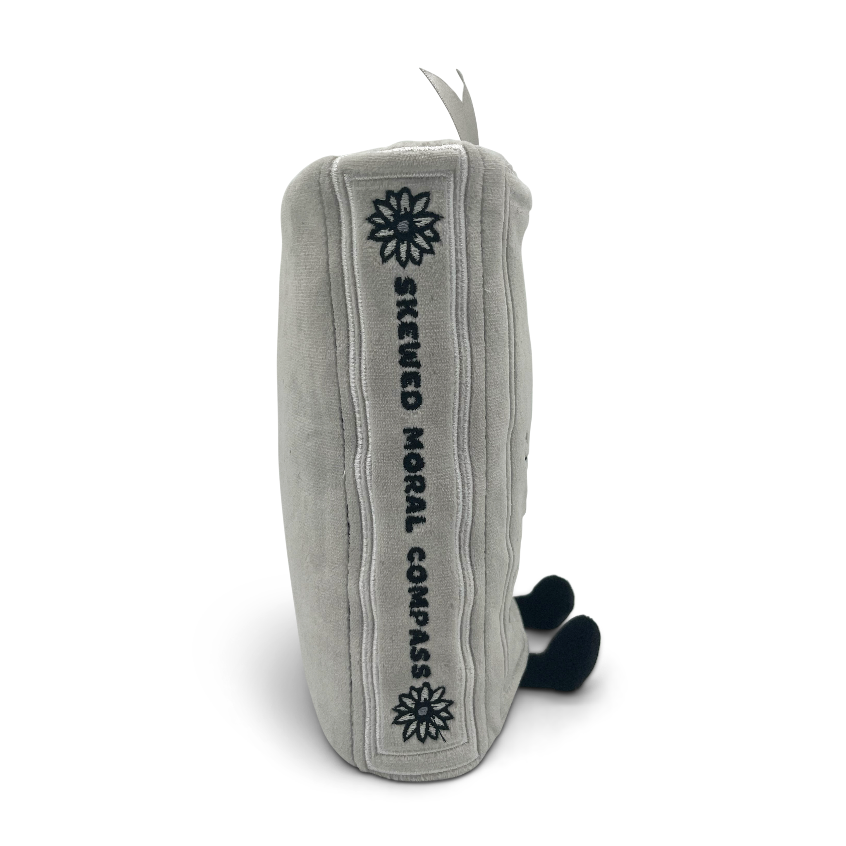 A book plush with the text 'skewed moral compass' embroidered on the side.
