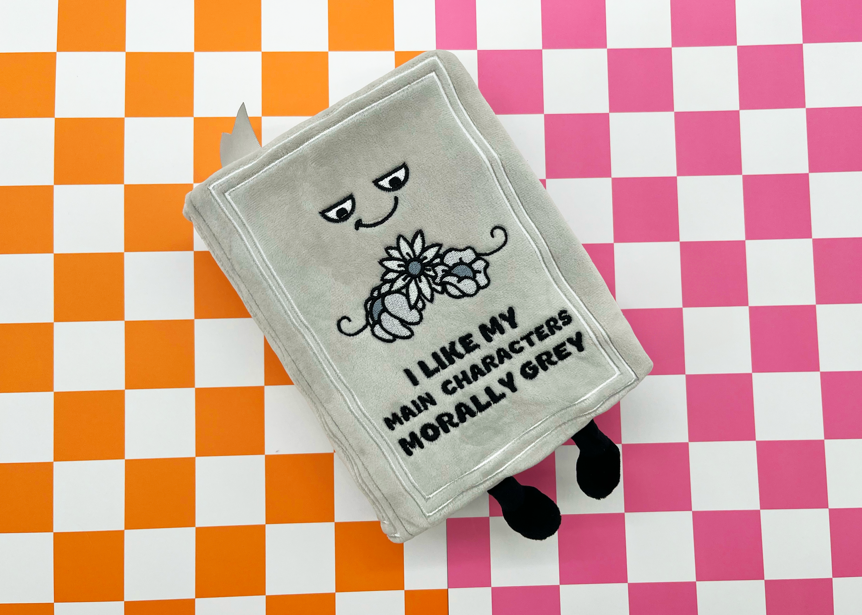 A gray plush book on a checkered background. 