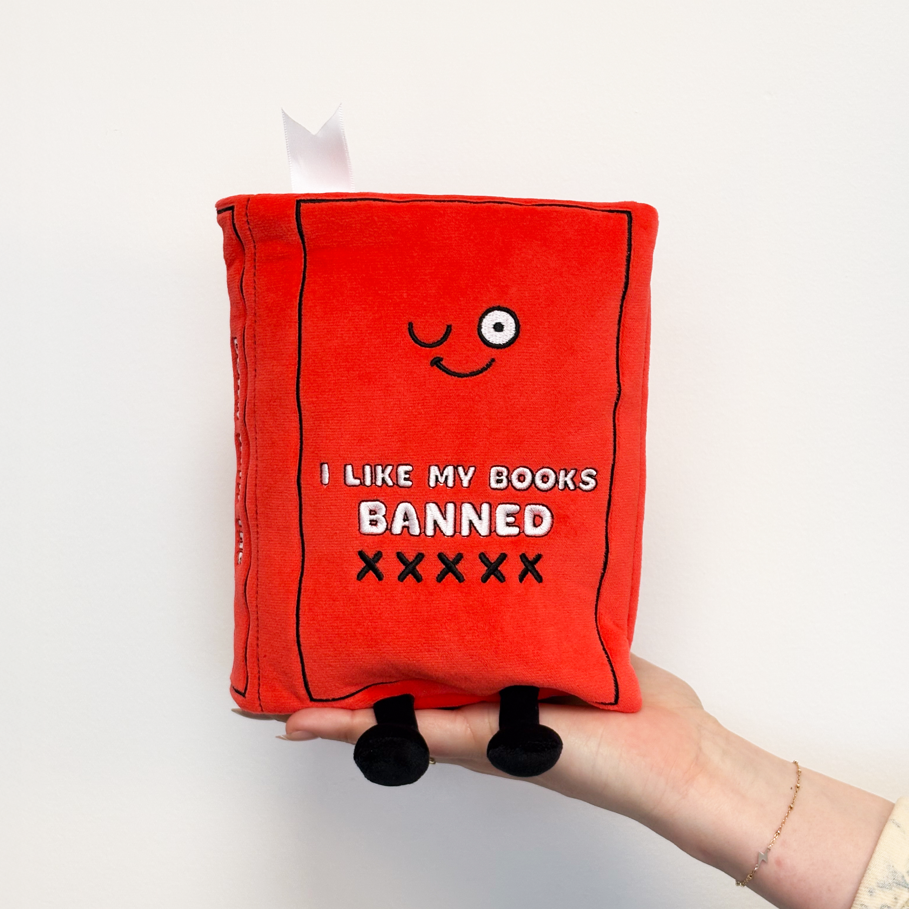 Hand holding red plush book with the text 'I LIKE MY BOOKS BANNED' on its cover.
