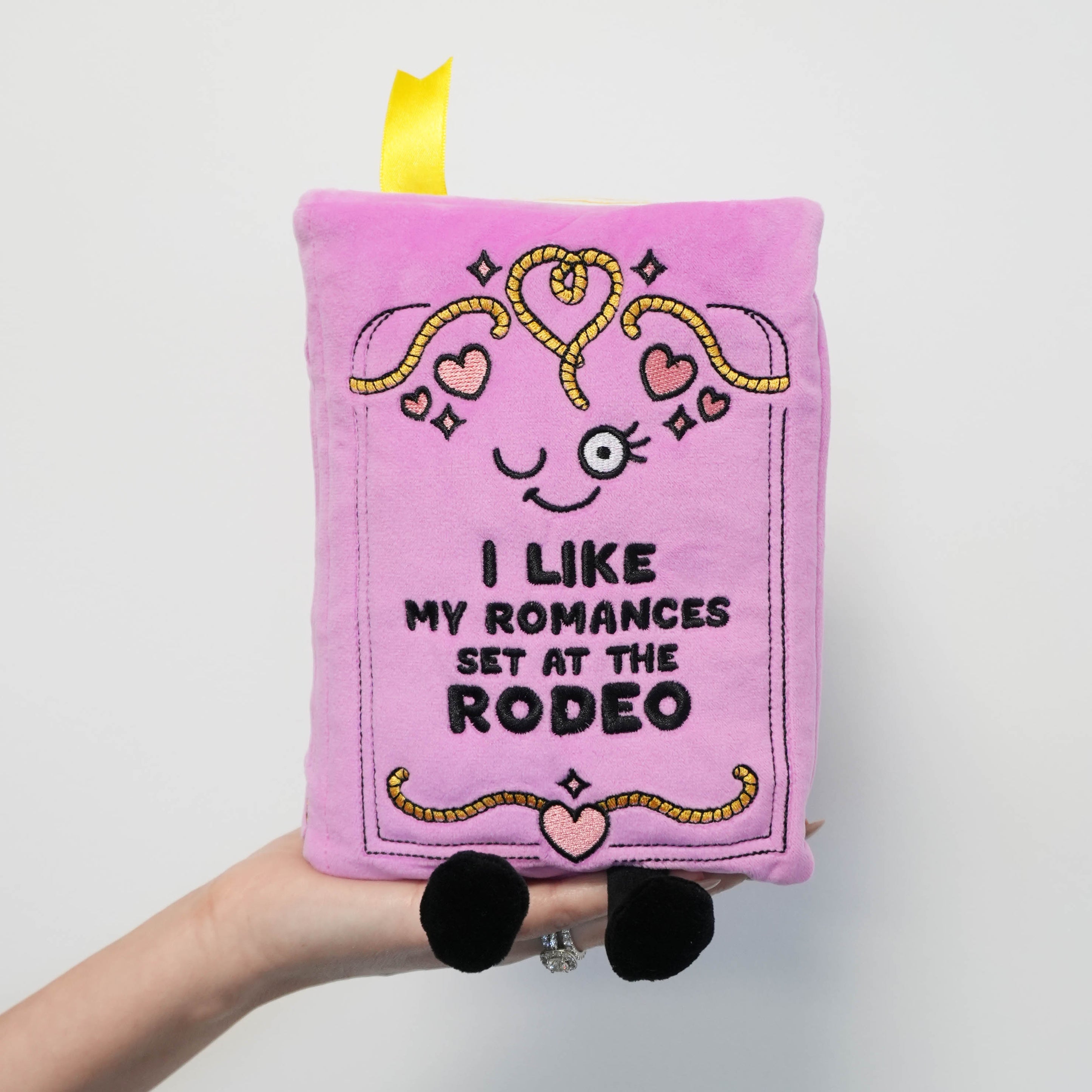 Pink plush book with text and heart designs held by a hand on a light gray background