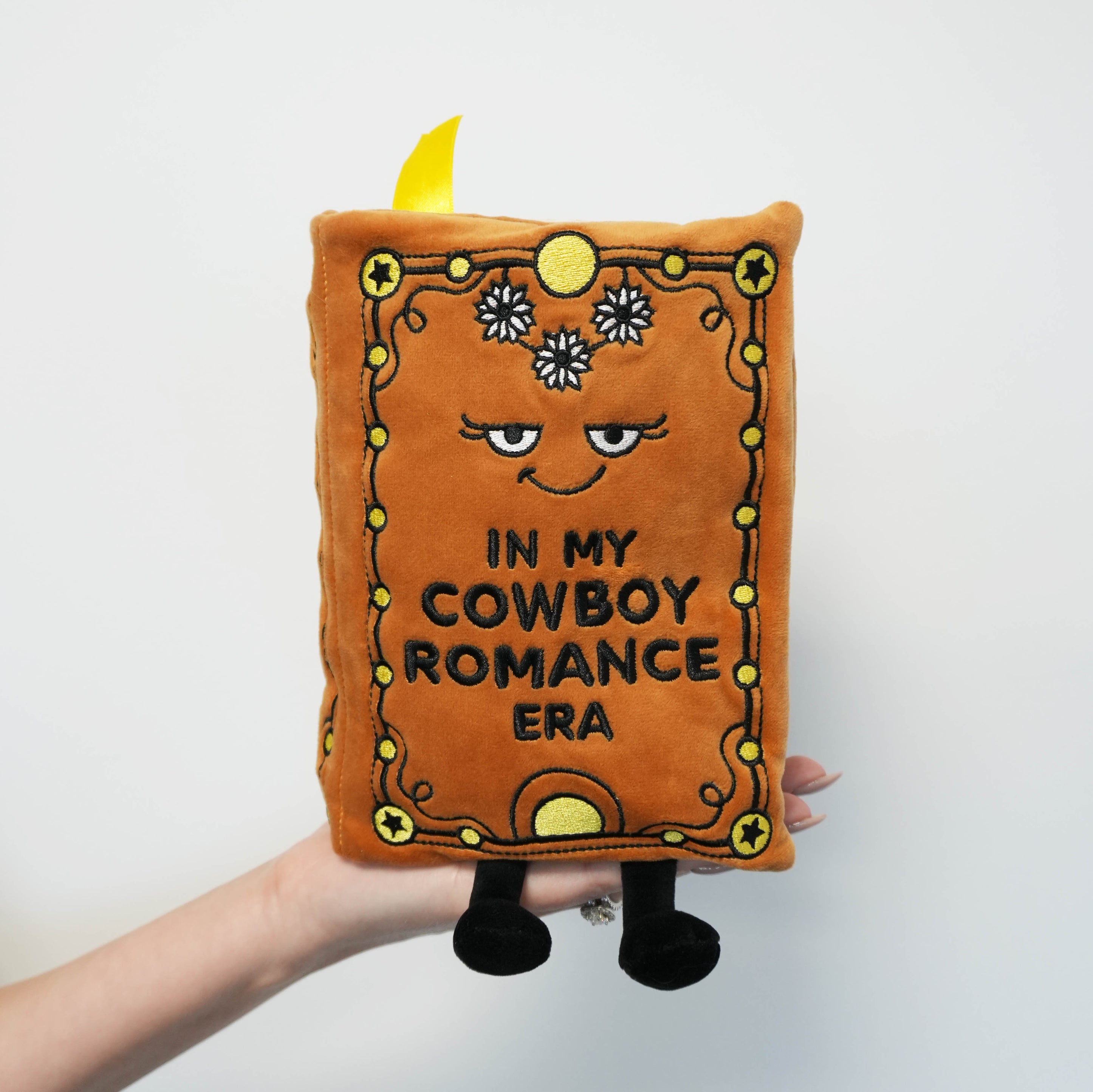 A brown book-shaped plush with a cowboy theme on a white background