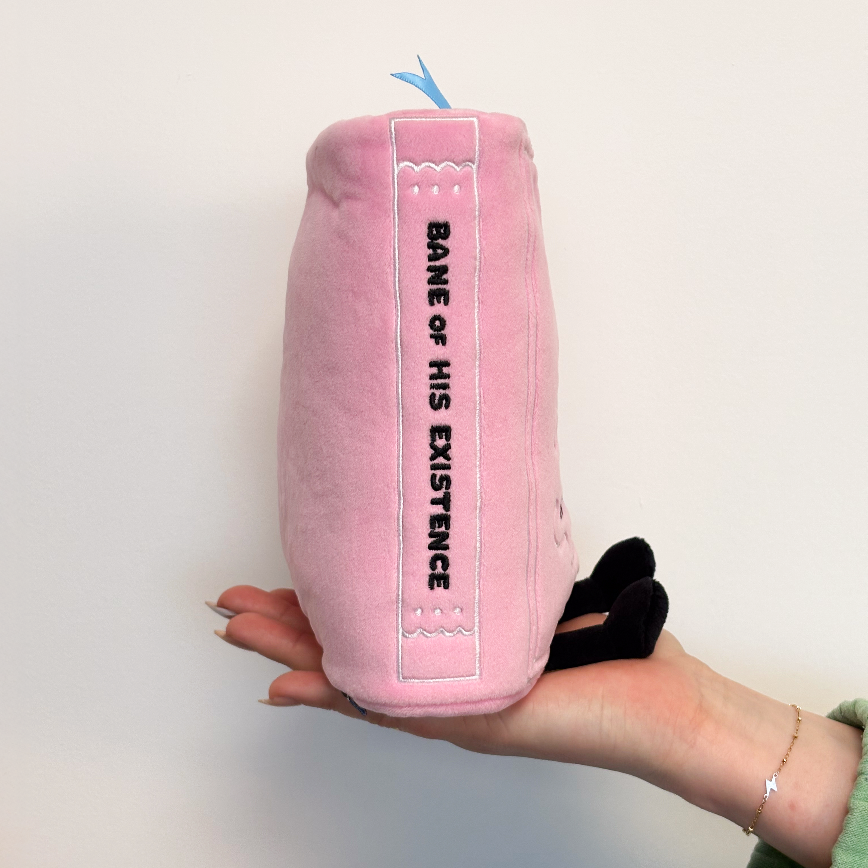 A plush book with a spine that reads "Bane of his existence." 