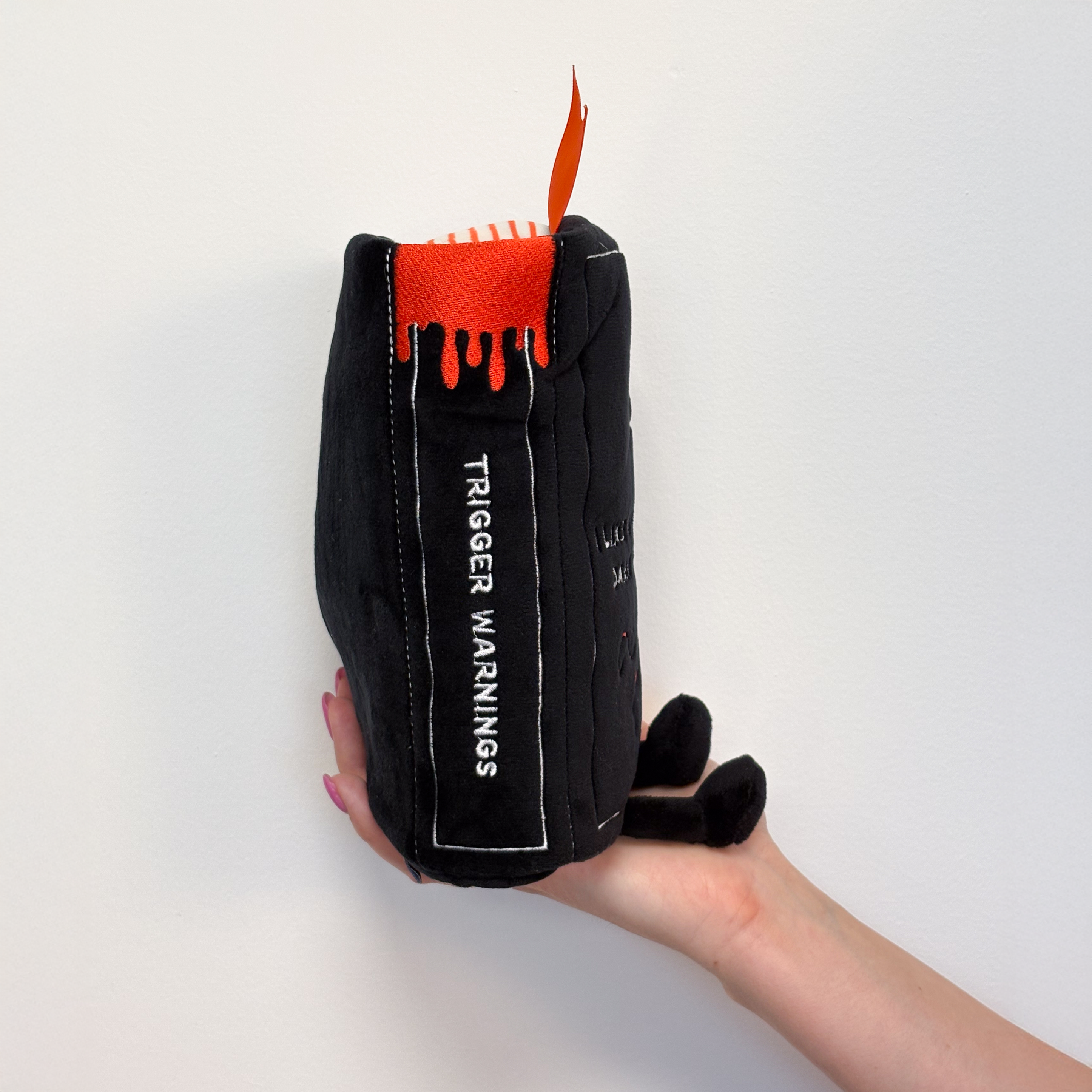 A hand holding a plush book with "trigger warning" written on the spine.