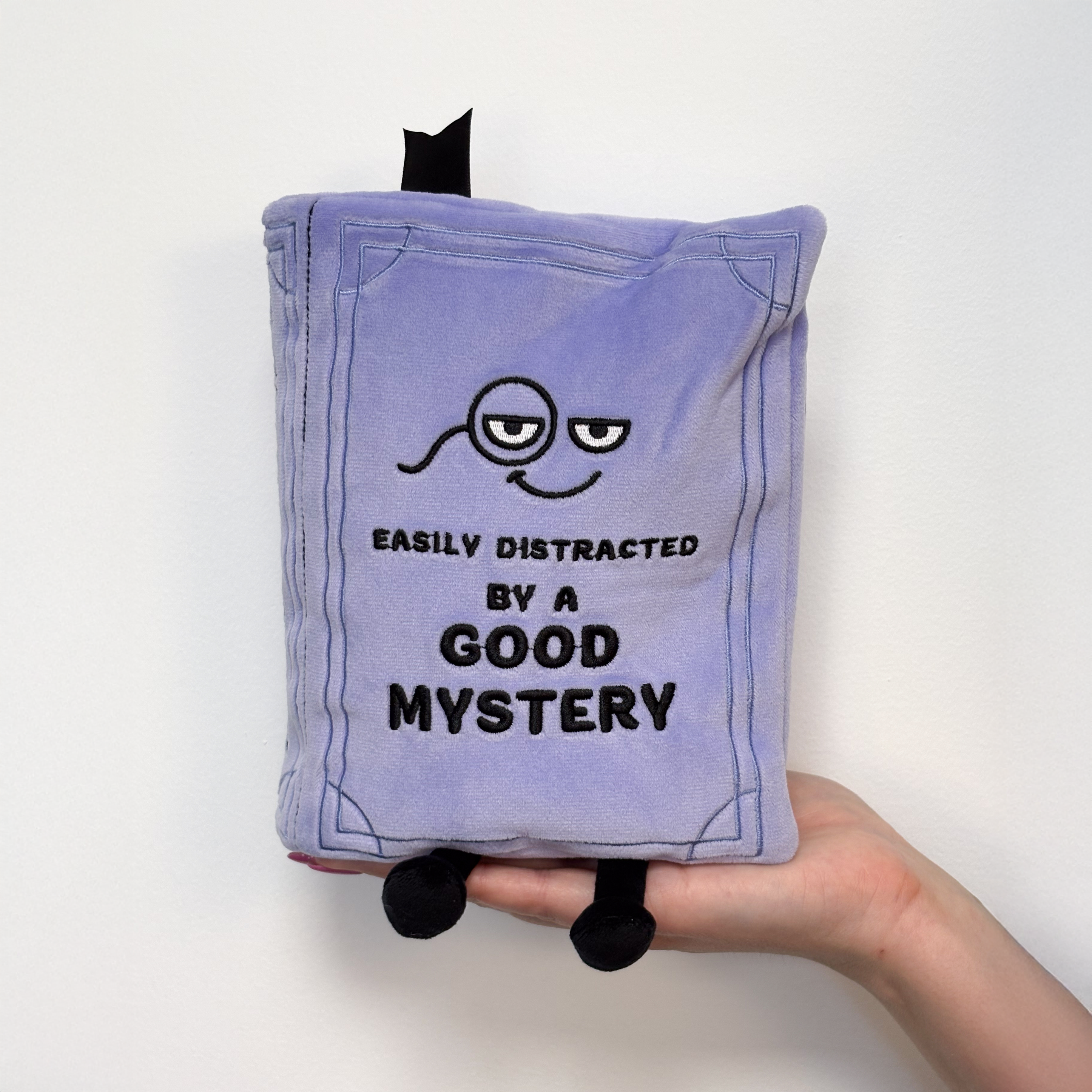 A hand holding a mystery book plush 