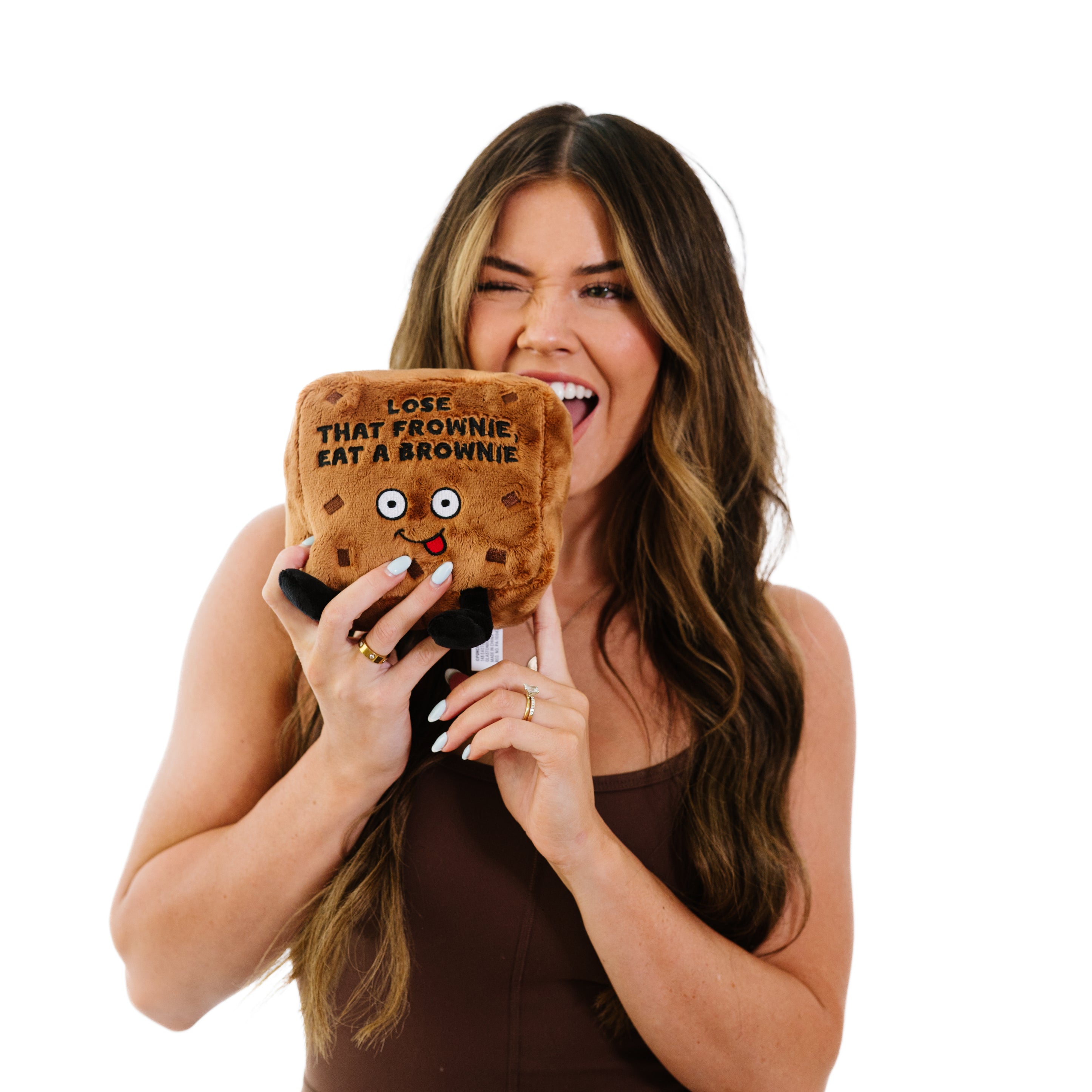 A model pretending to bite a plush designed to look like a brownie with a smiling face and the text 'LOSE THAT FROWNIE, EAT A BROWNIE' on it.
