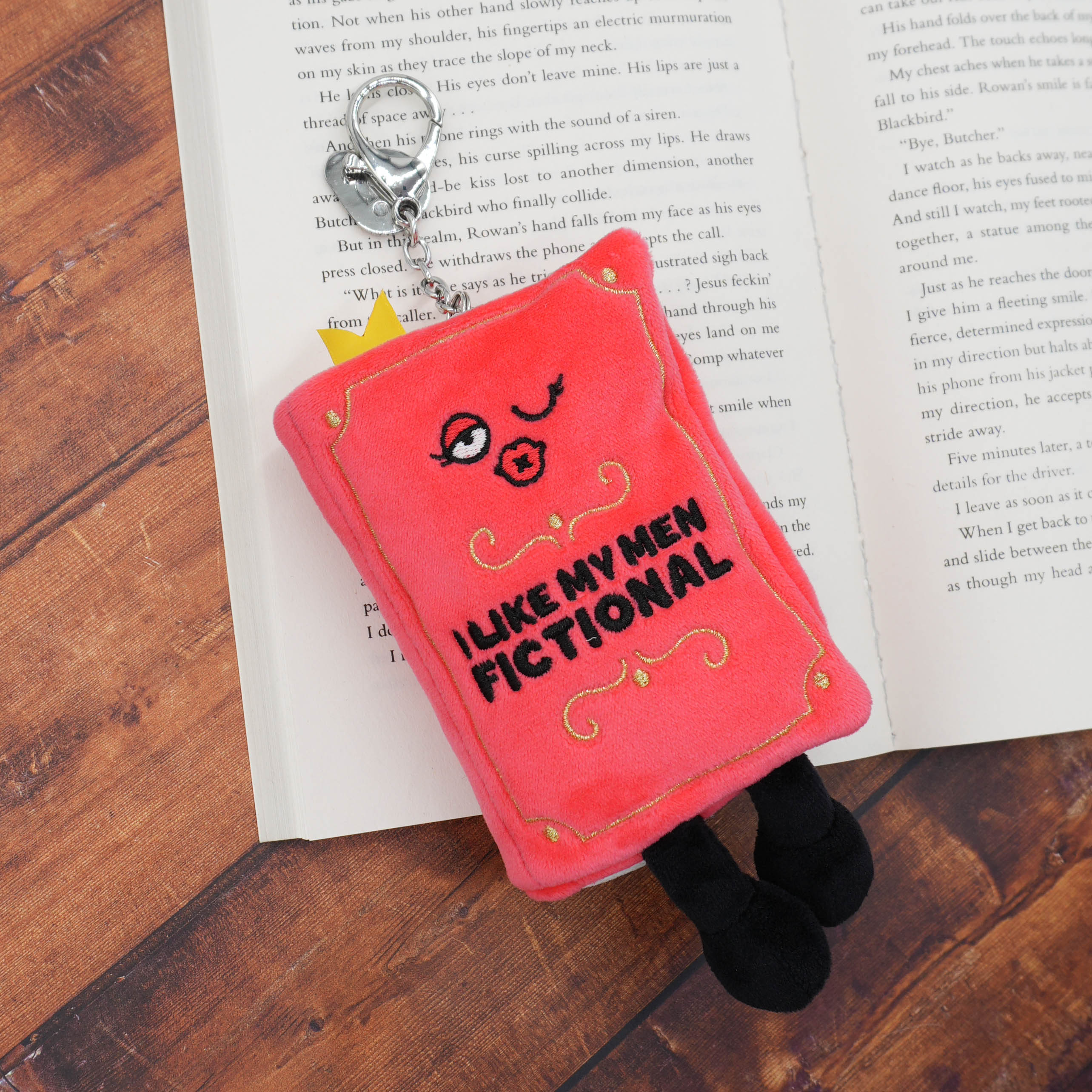 Red plush book bag charm with character design and text on an open book