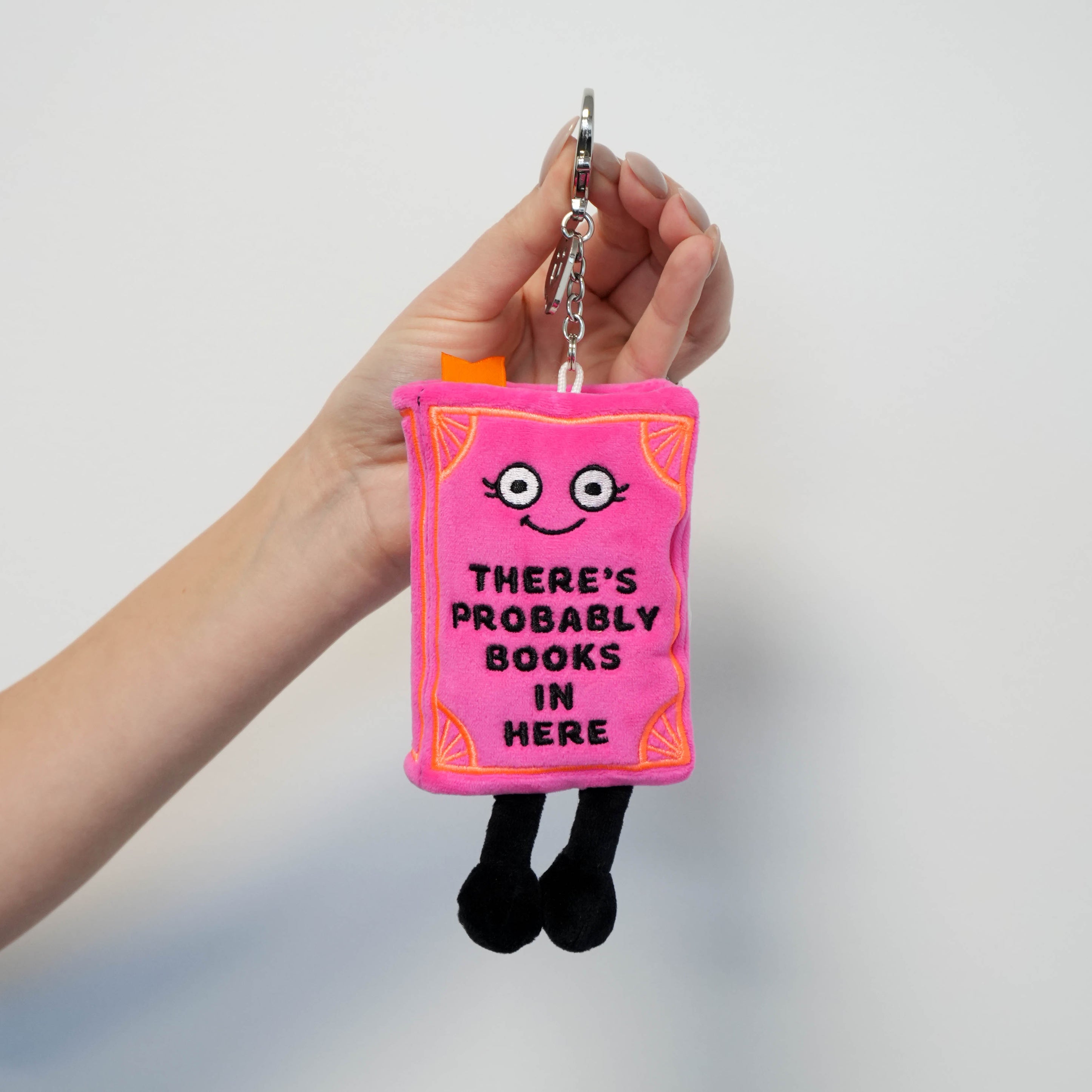 Pink plush keychain shaped like a book with text held by a hand against a plain background