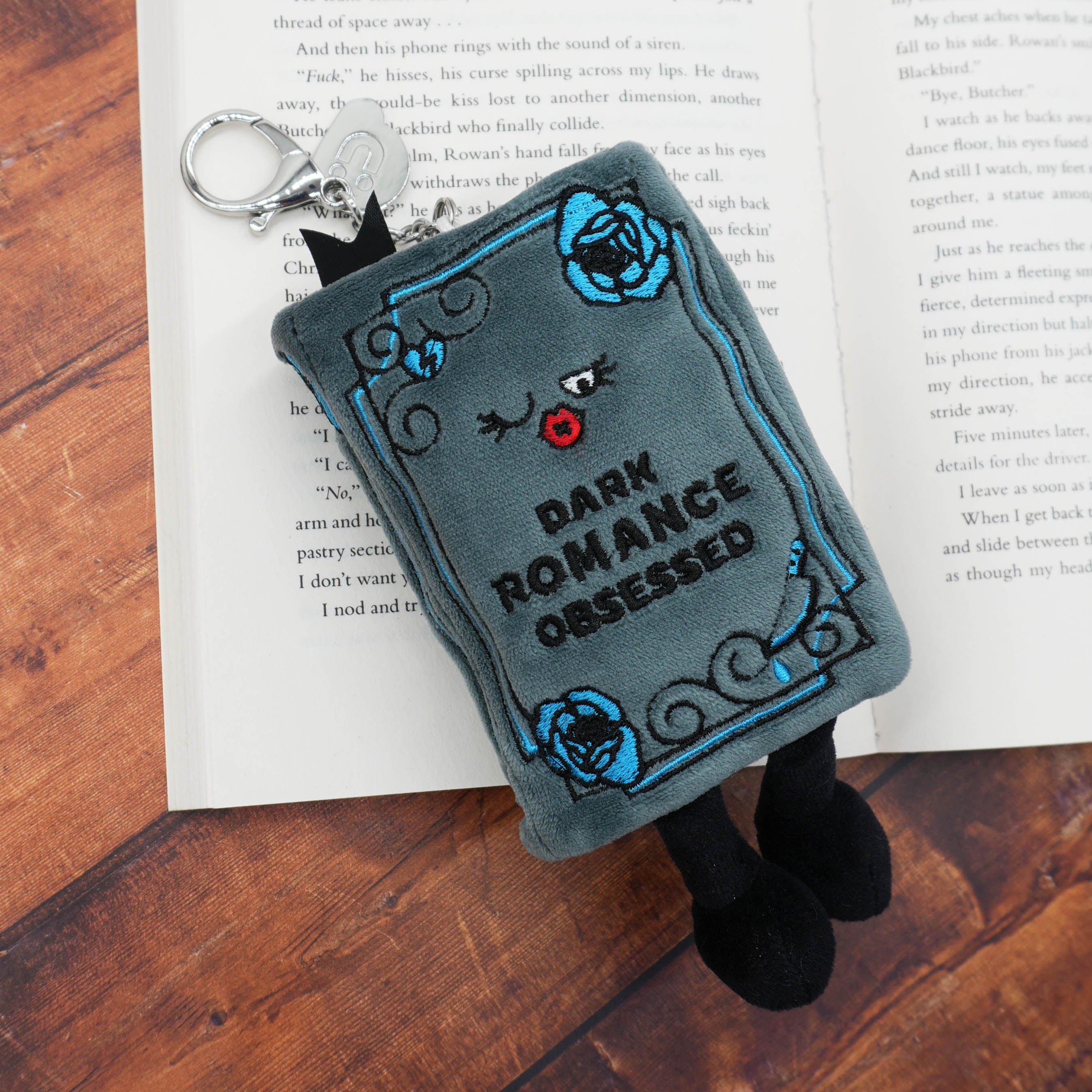Plush bag charm shaped like a book with 'Dark Romance Obsessed' text on an open book.