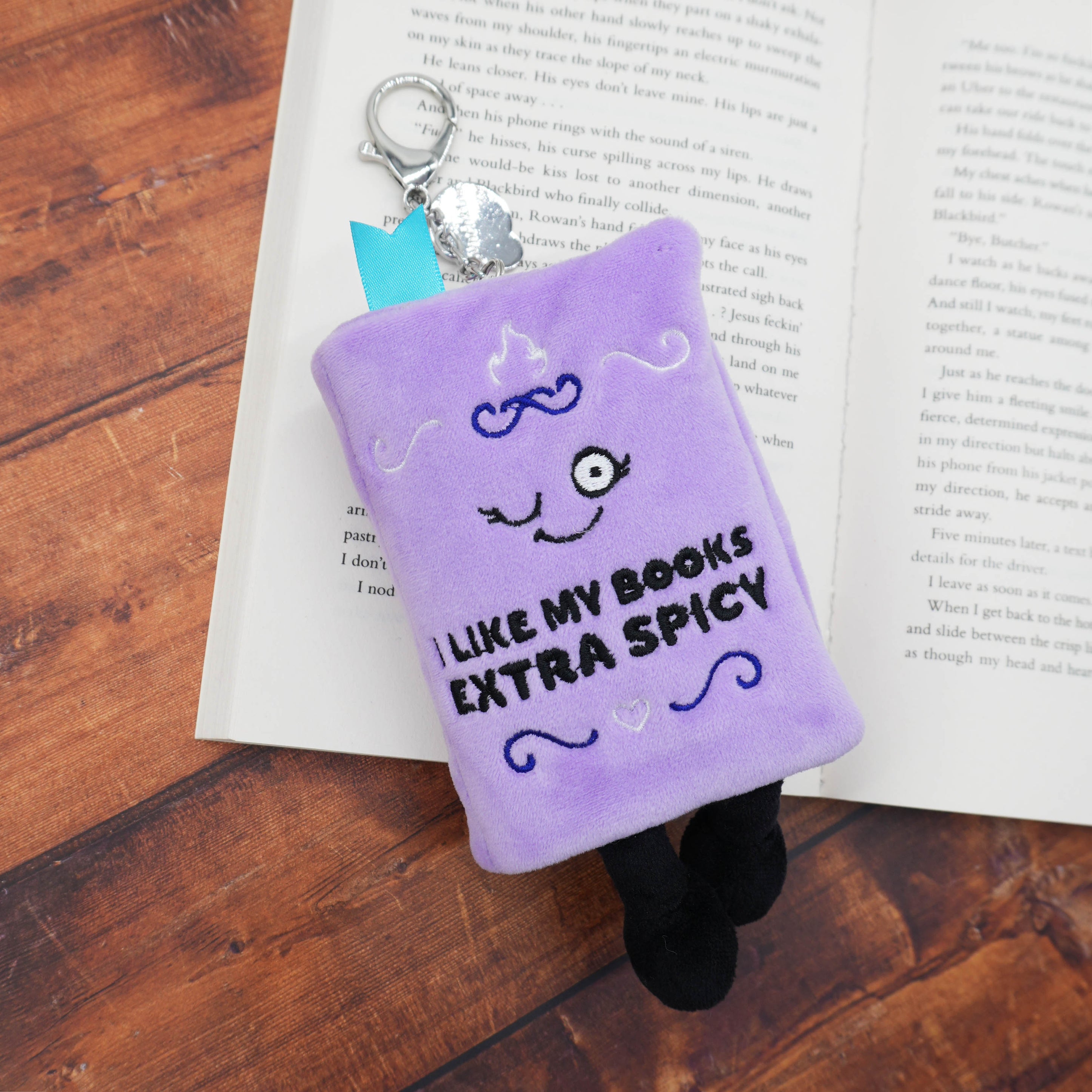 Purple plush book charm with 'I like my books extra spicy' text on an open book.