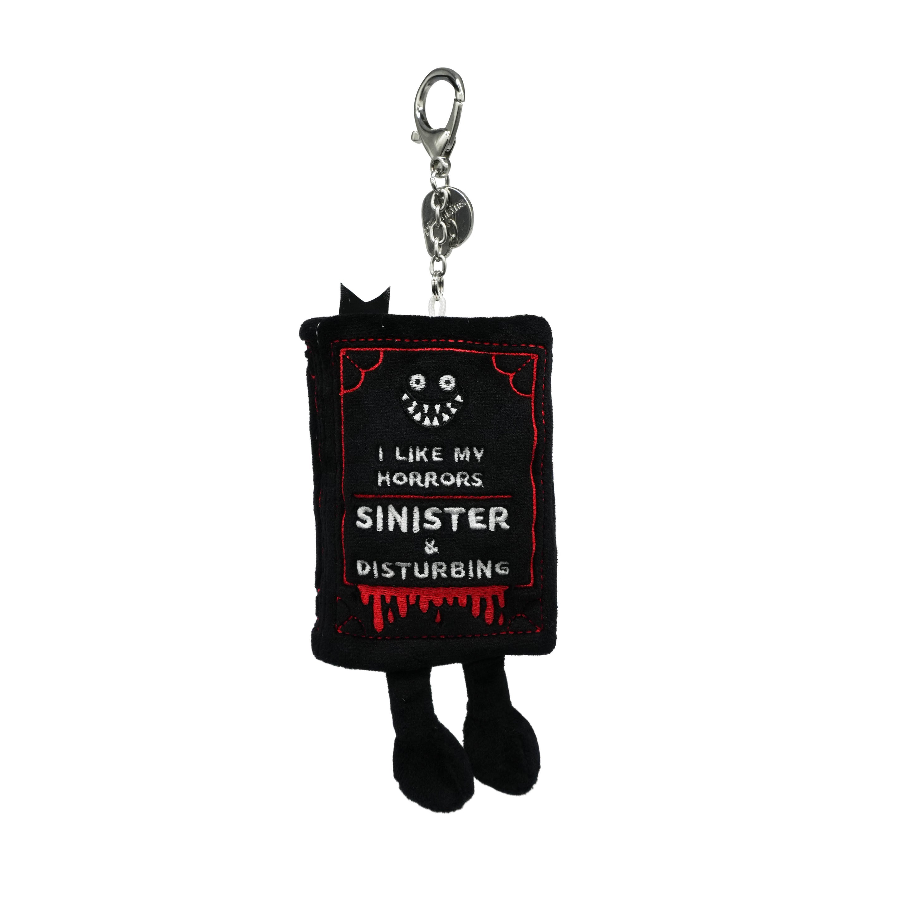 Black bag charm shaped like a book with text 'I like my horrors sinister and disturbing' on a white background