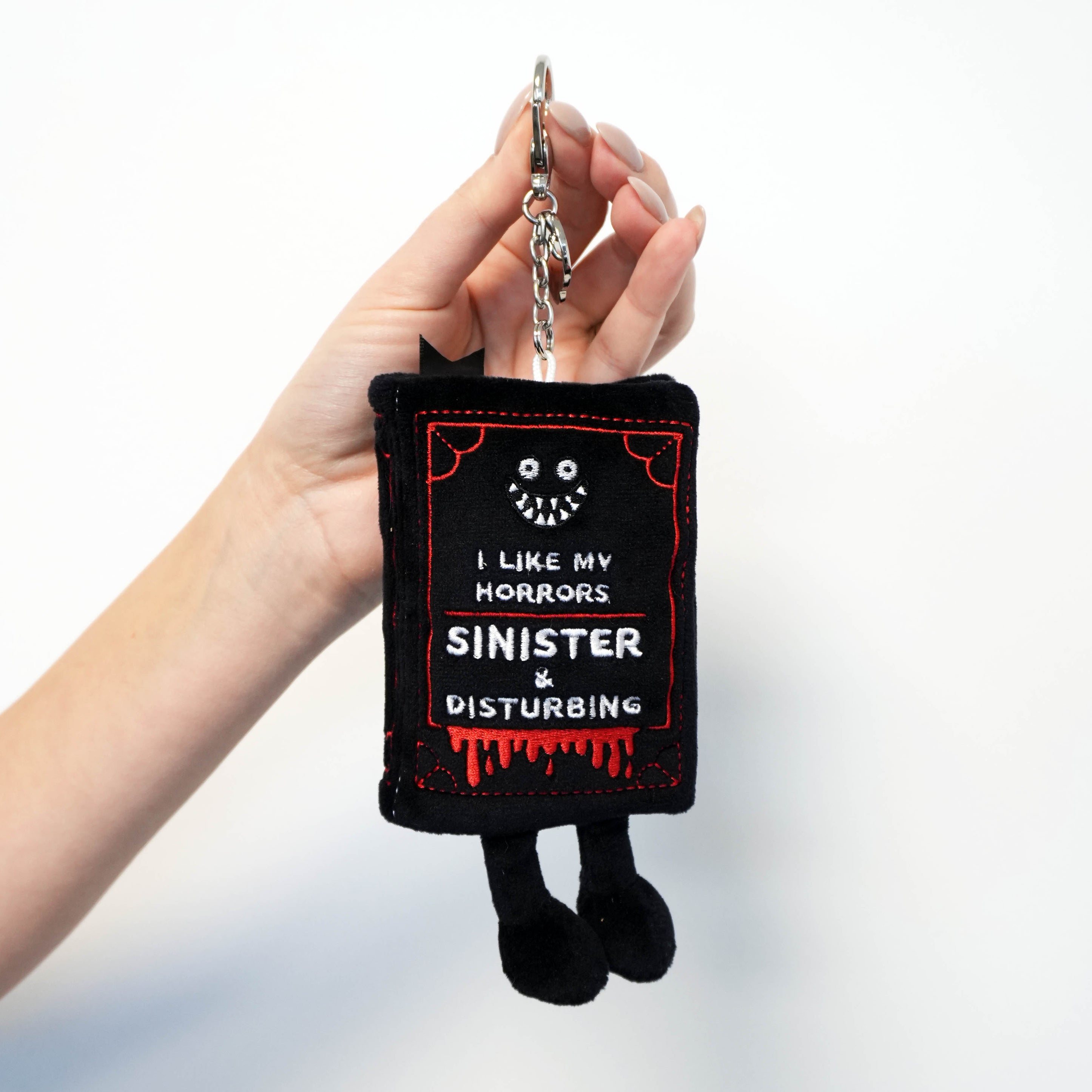Hand holding black horror-book bag charm against a white background