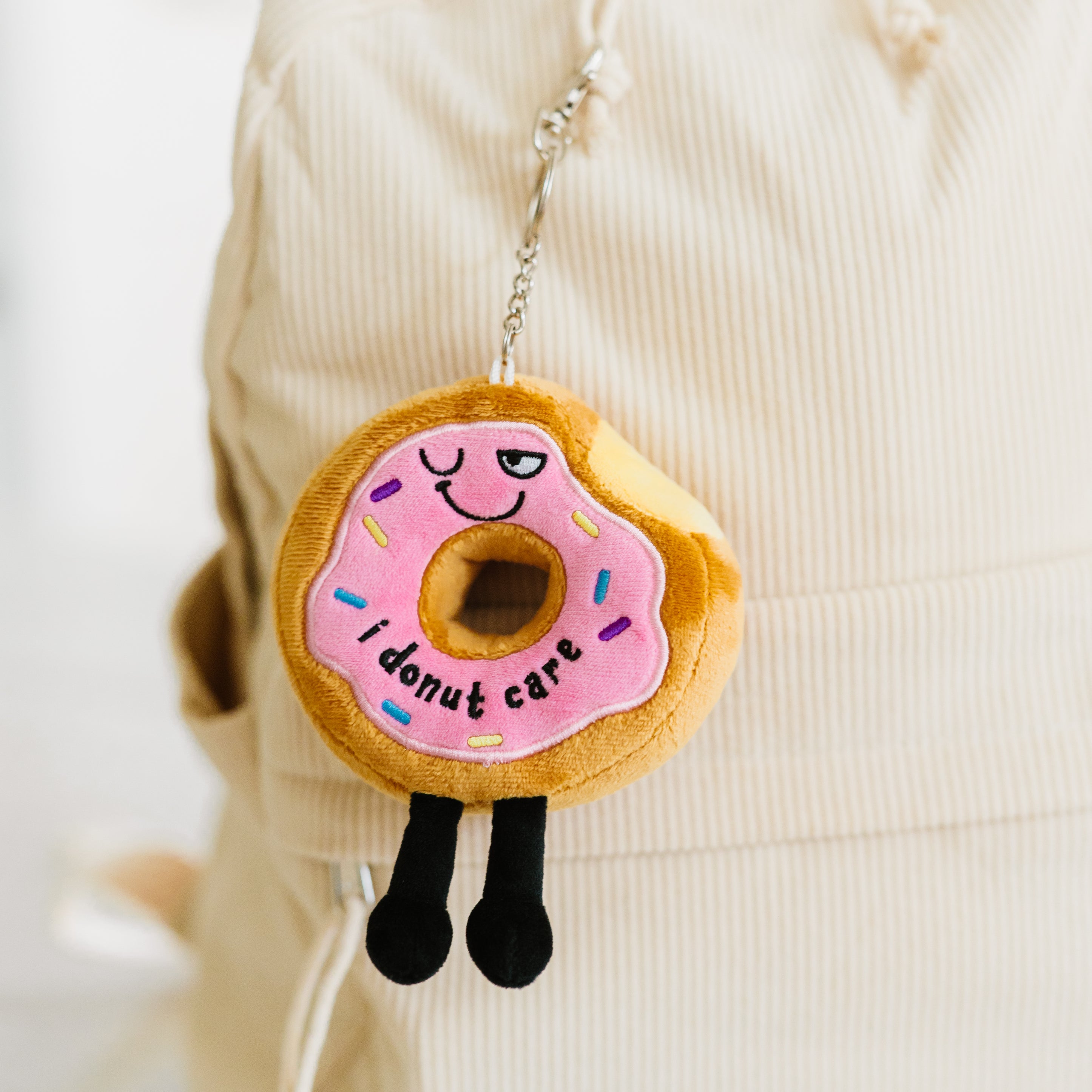 A plush shaped like a donut with the phrase 'I DONUT CARE' written on it hanging off a backpack.