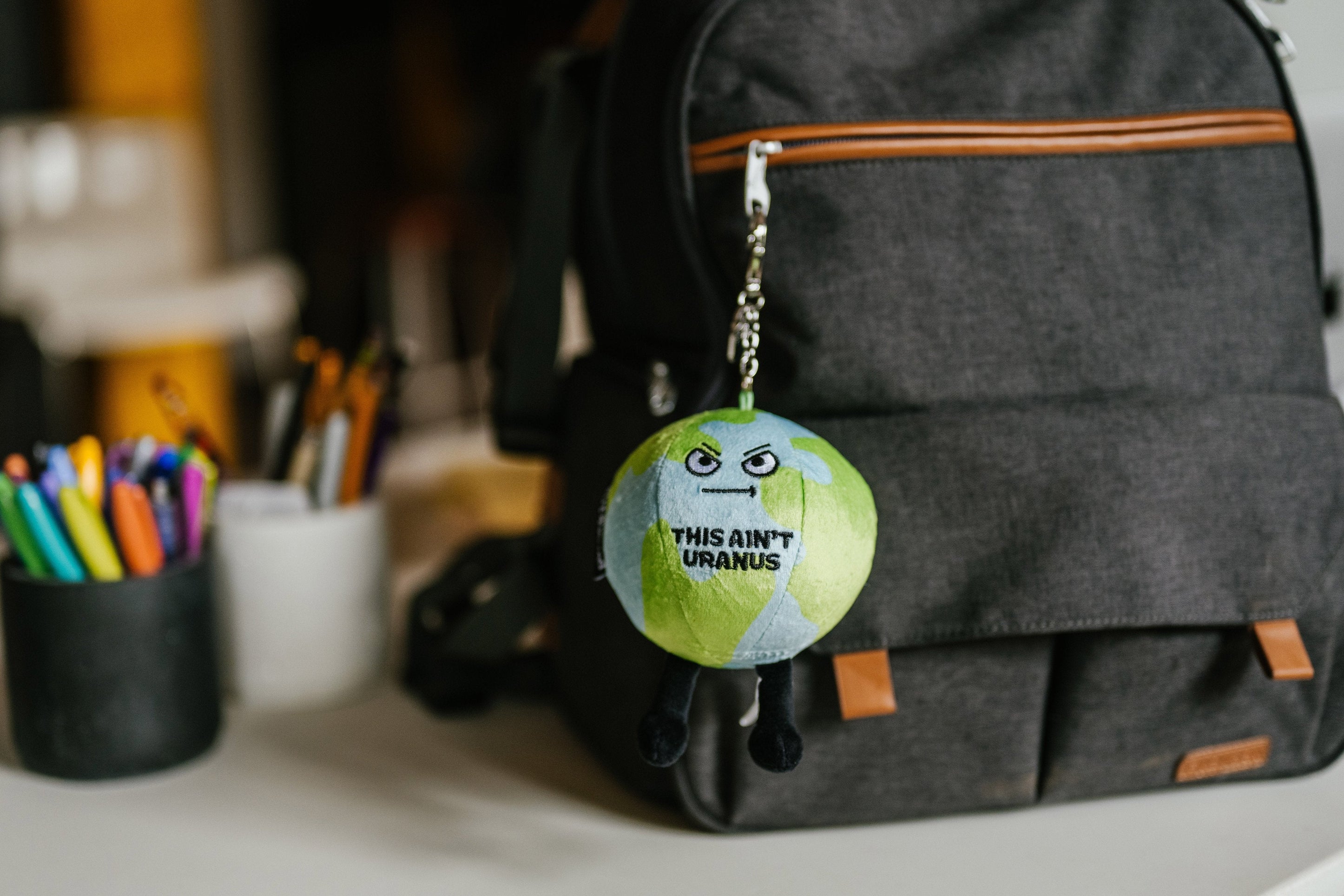 A bag charm designed to resemble the Earth with the saying 'This ain't Earth' hanging on a backpack.
