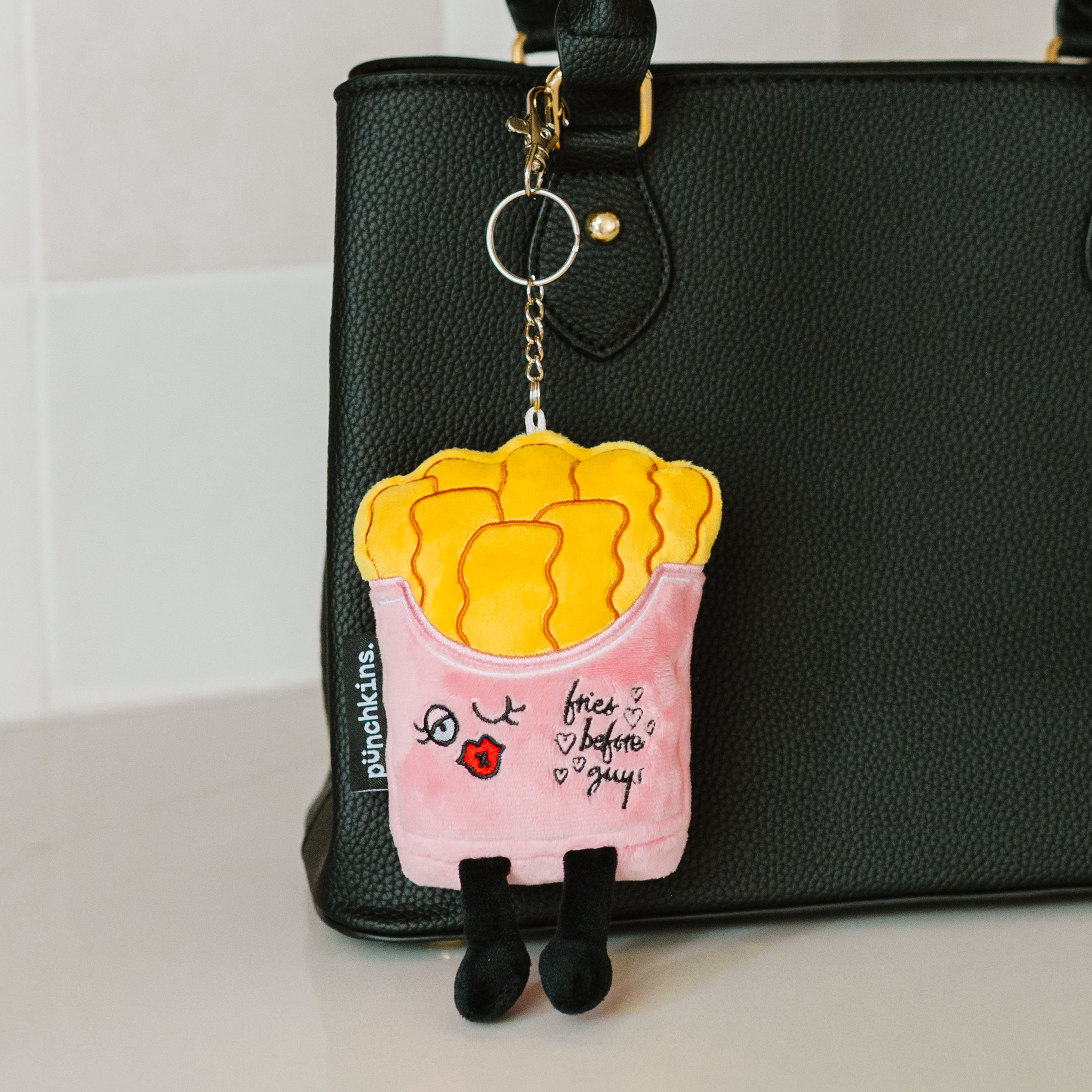 A plush bag charm designed to look like a carton of French fries with eyes and the text 'Fries Before Guys'.