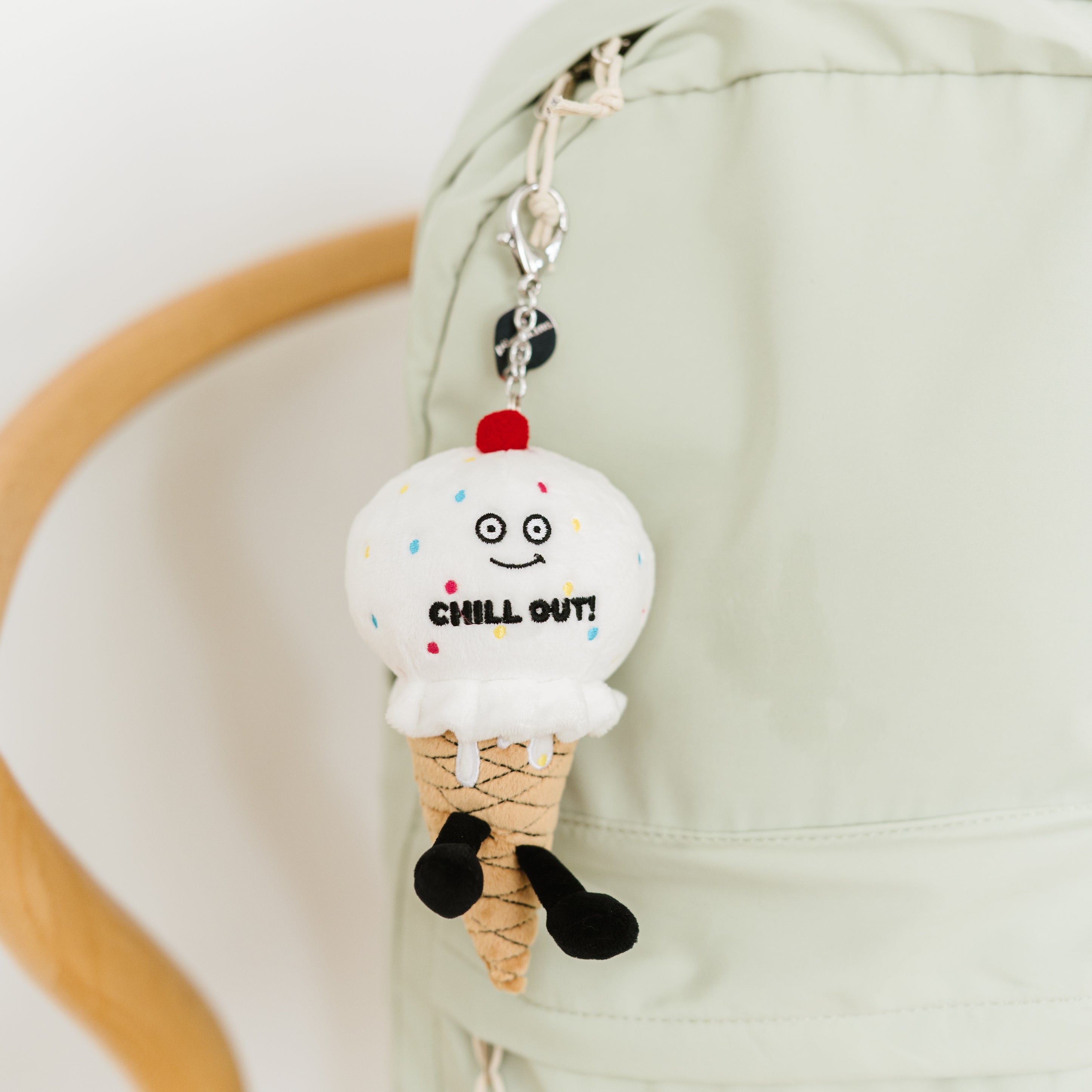 A plush shaped like an ice cream cone with a face, cherry on top, and sprinkles, with the text 'CHILL OUT!' written on it hanging on a bag charm.