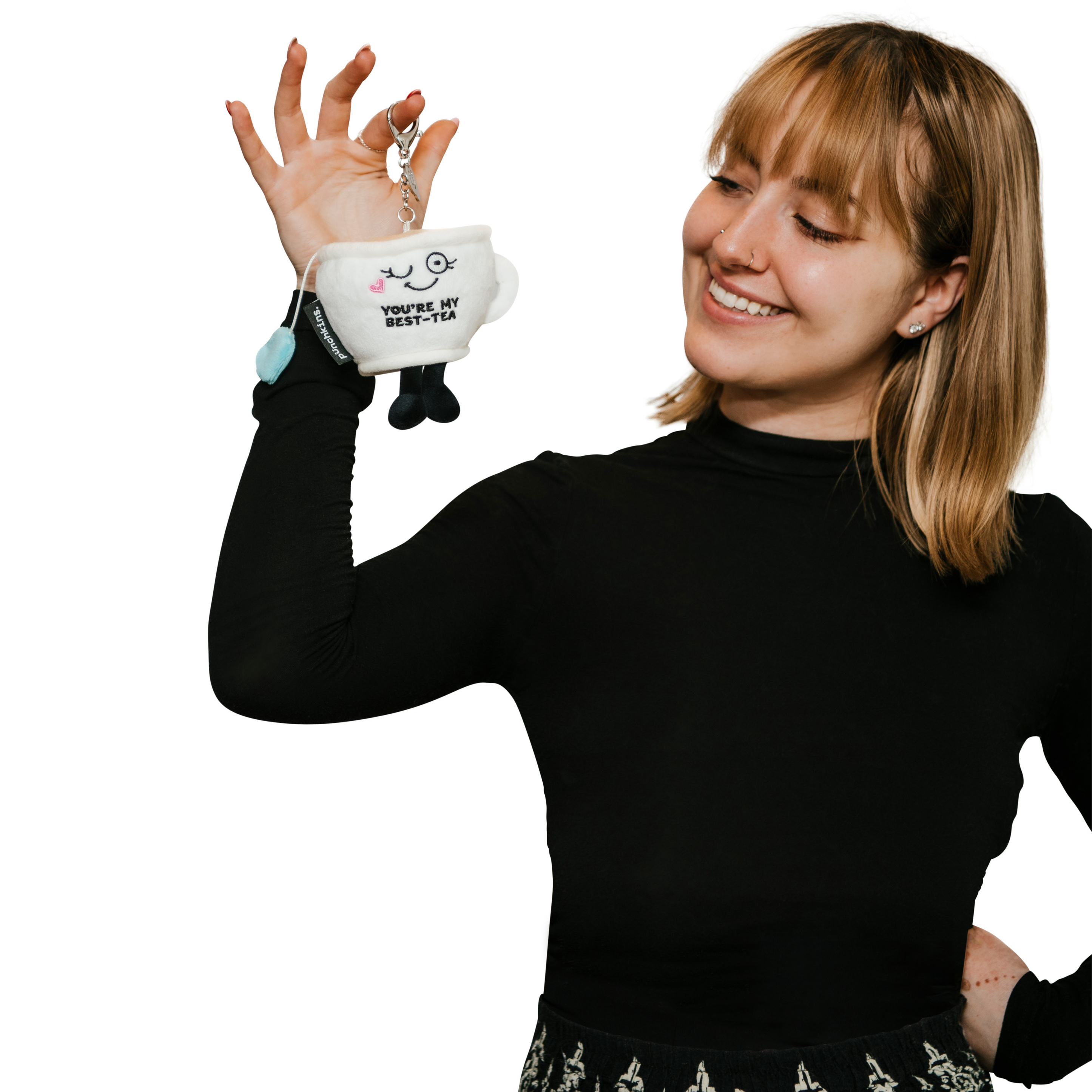 A woman holding a plush teacup bag charm with a cute face and 'you're my best-tea' text embroidered on it.