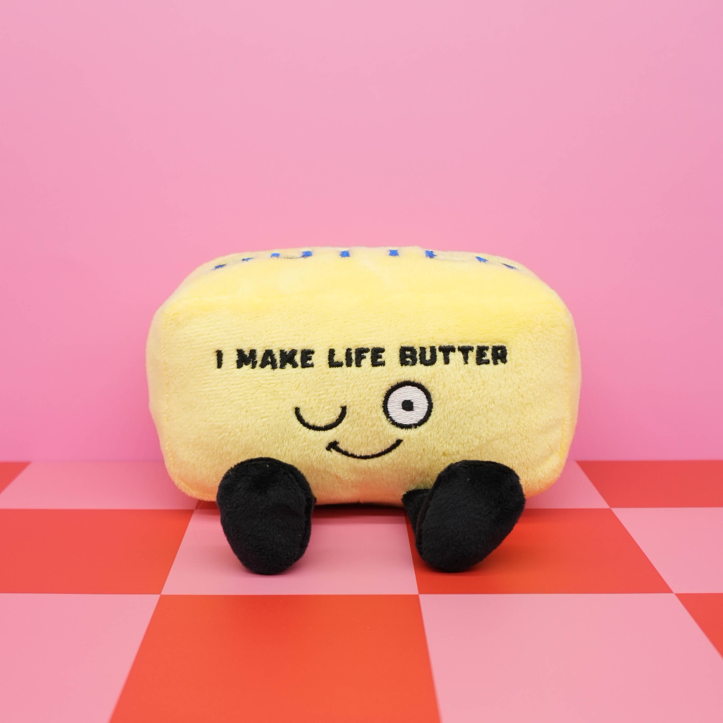 Plush butter toy with text on a pink and red checkered background