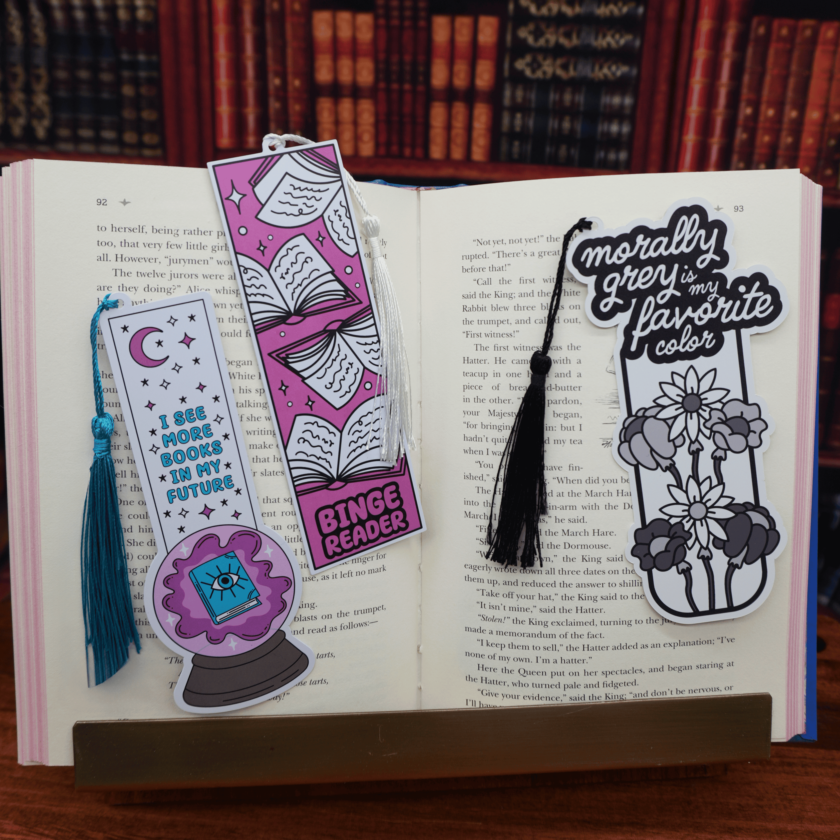 Open book with various bookmarks featuring tassels on a wooden surface.