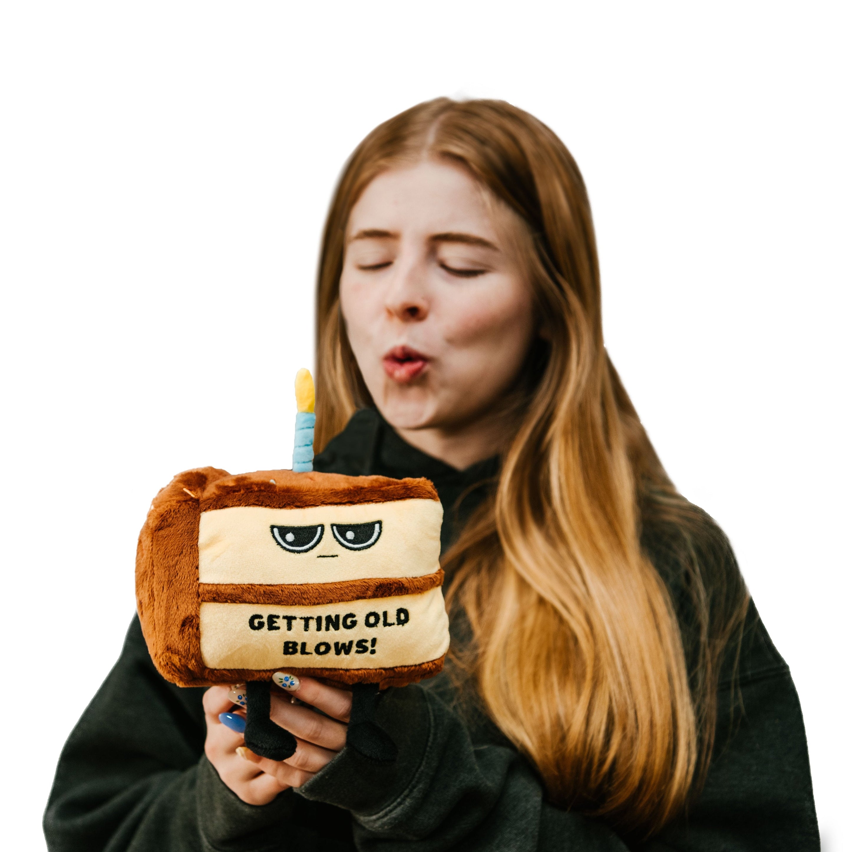 A model holding a plushie designed to look like a piece of birthday cake with a grumpy face and text on it that reads, 'GETTING OLD BLOWS!'