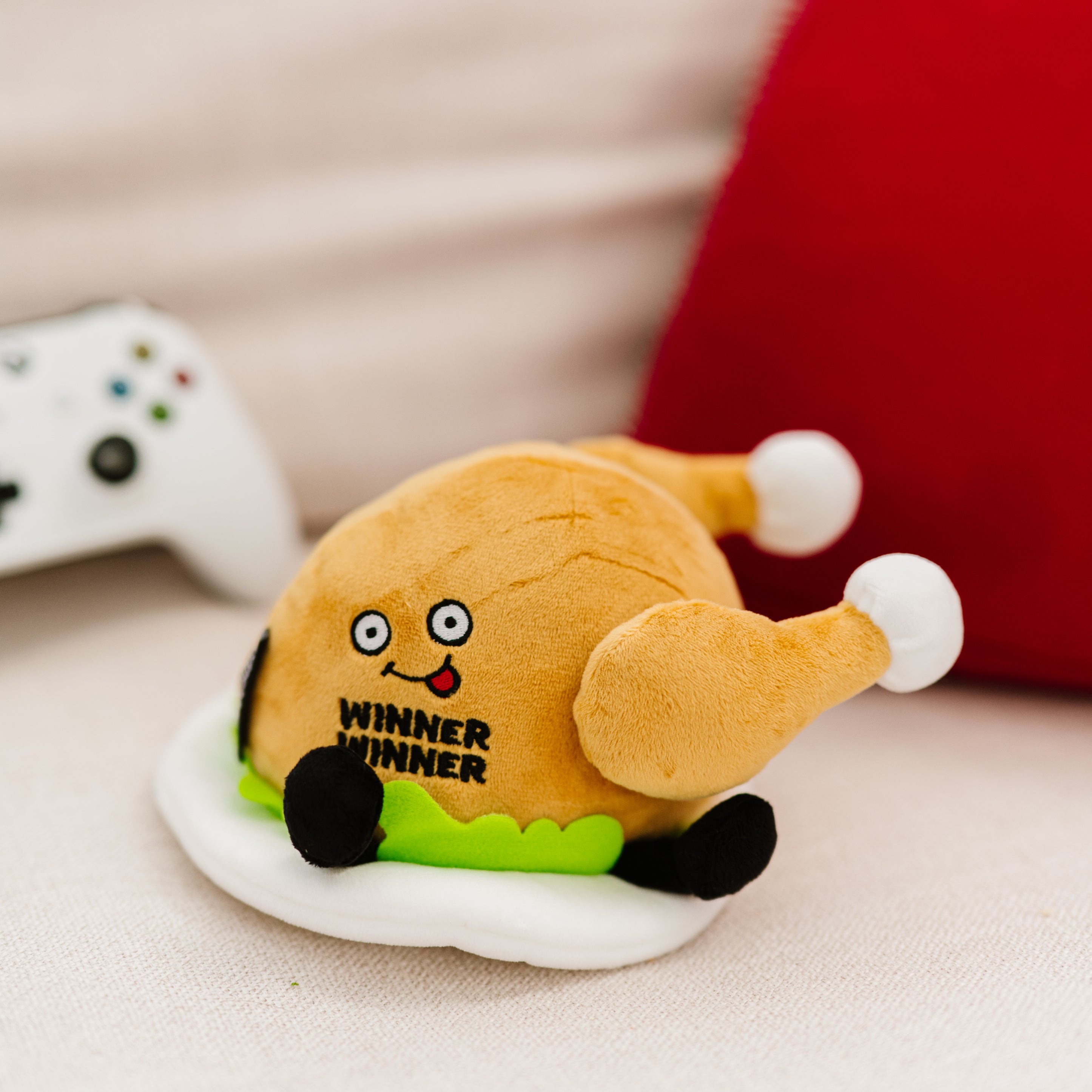 A plush designed to look like a roasted chicken with a 'Winner Winner' text on its placed on a couch.
