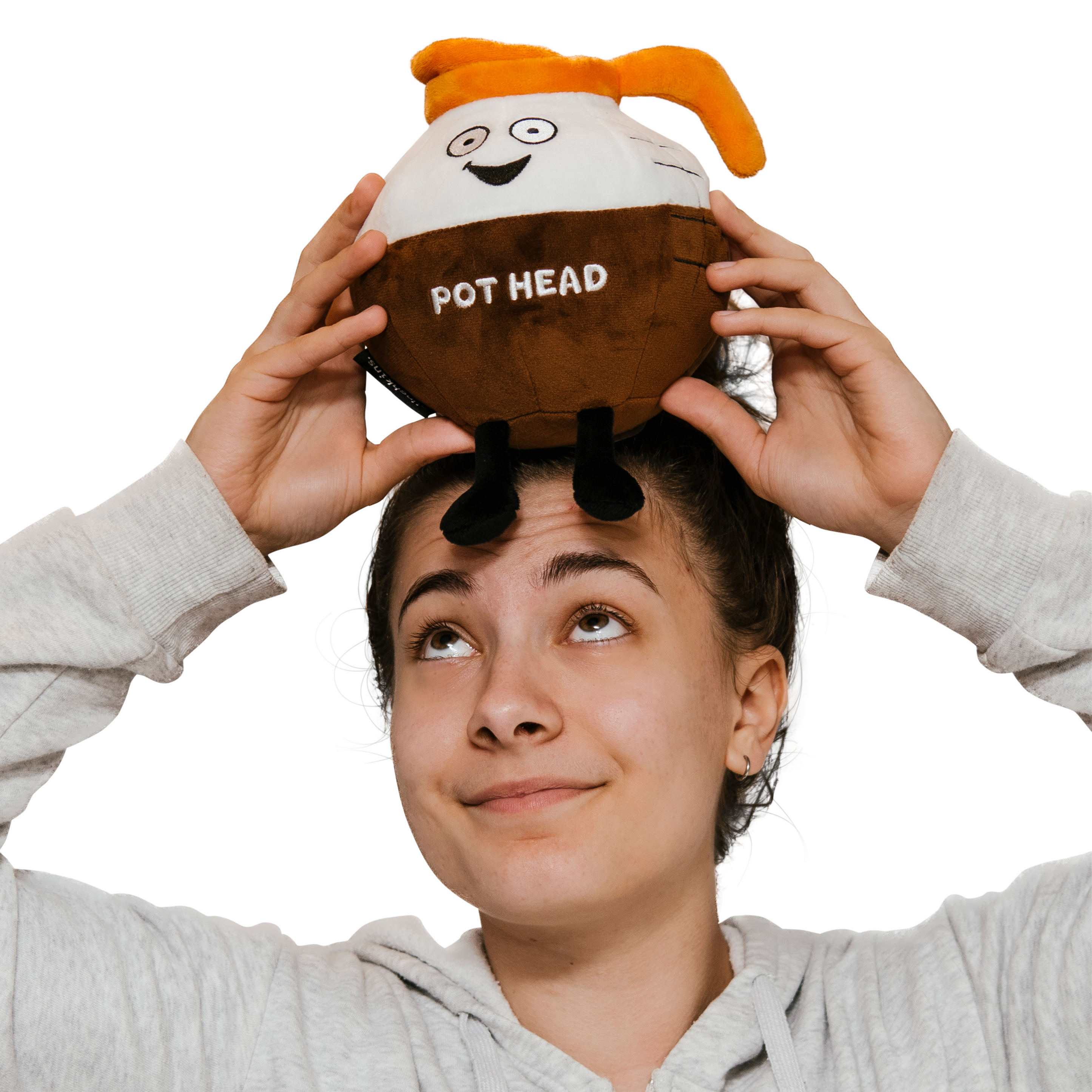 A woman holding a plush designed to resemble a coffee pot with a smiling face and the text 'POT HEAD' on it.