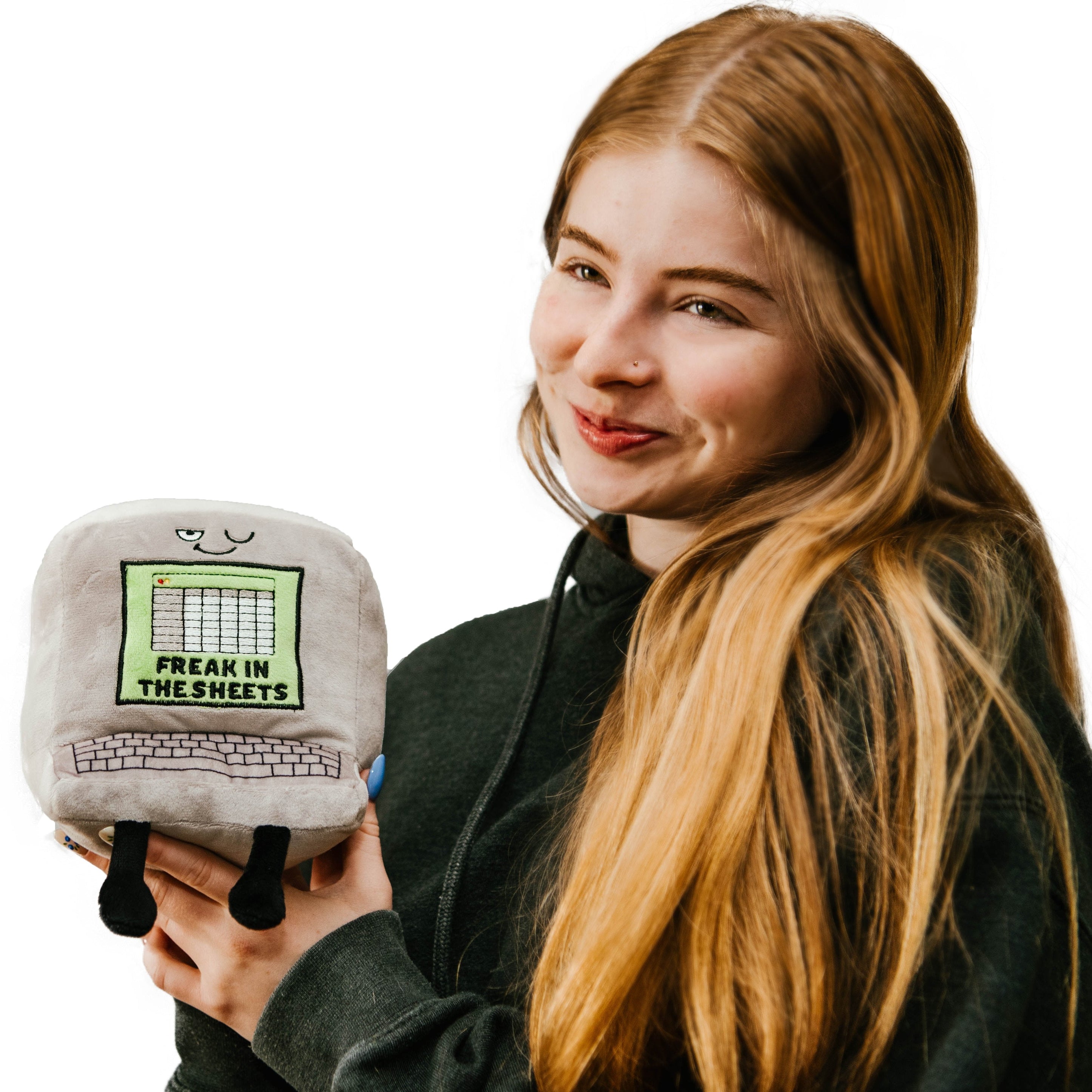 A model holding a plushie designed to resemble a computer with the text 'Freak in the Sheets' on a spreadsheet, with a playful expression and dangling feet.