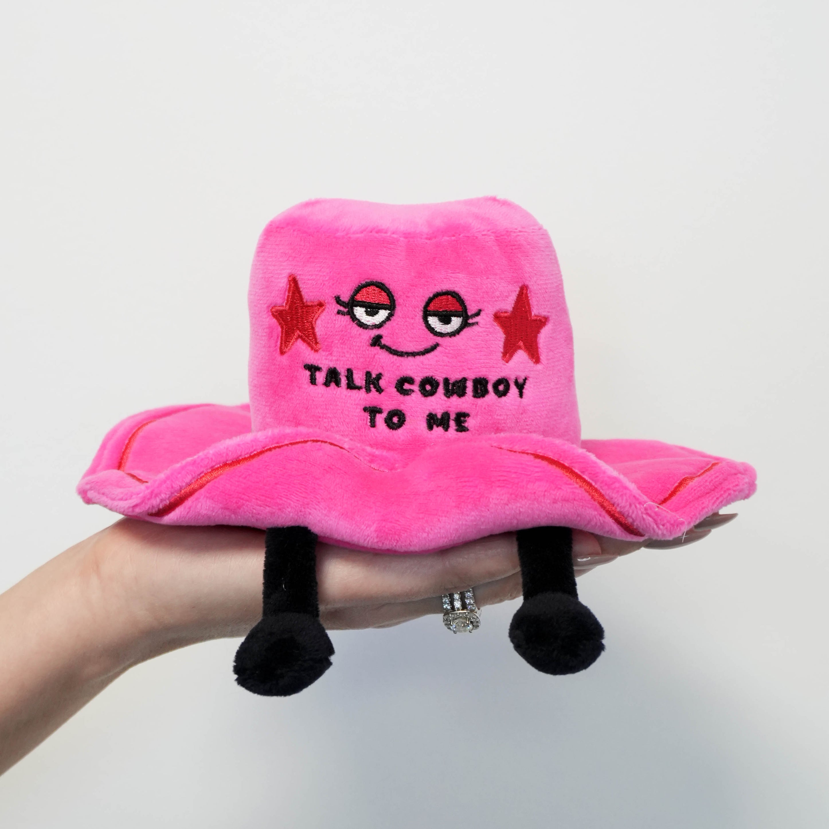 A hand holding a pink plush toy with cowboy hat and 'Talk Cowboy to Me.' 