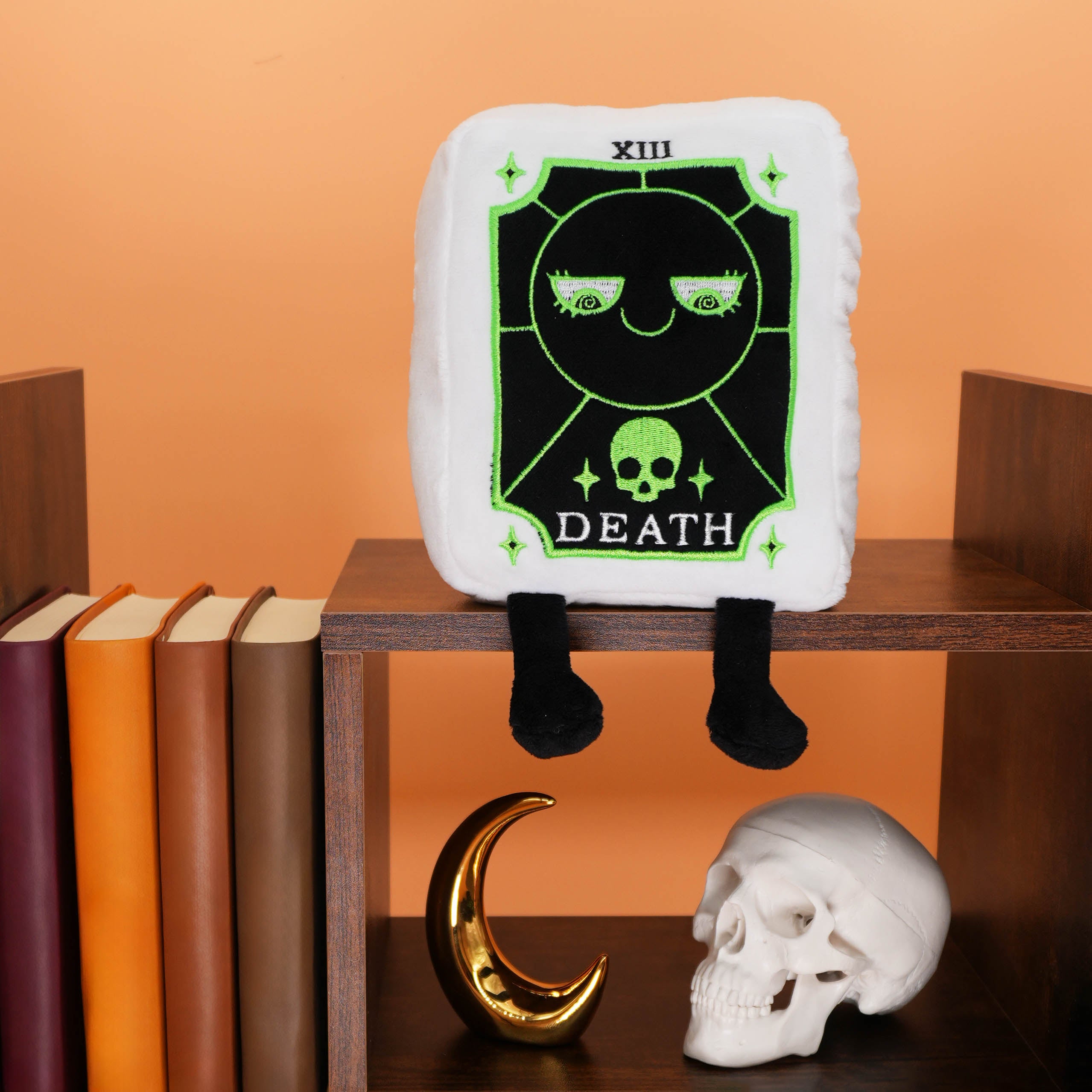 Plush toy resembling a Death Tarot Card from a tarot set on a shelf with books and decorative items.