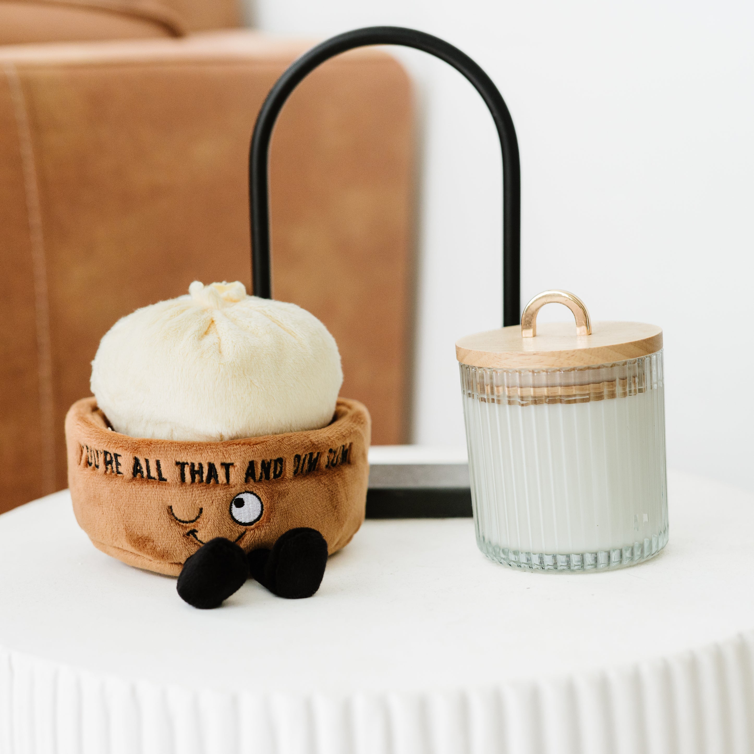 A plush dim sum soup dumpling with a smiling face and dangling legs placed on a table. 