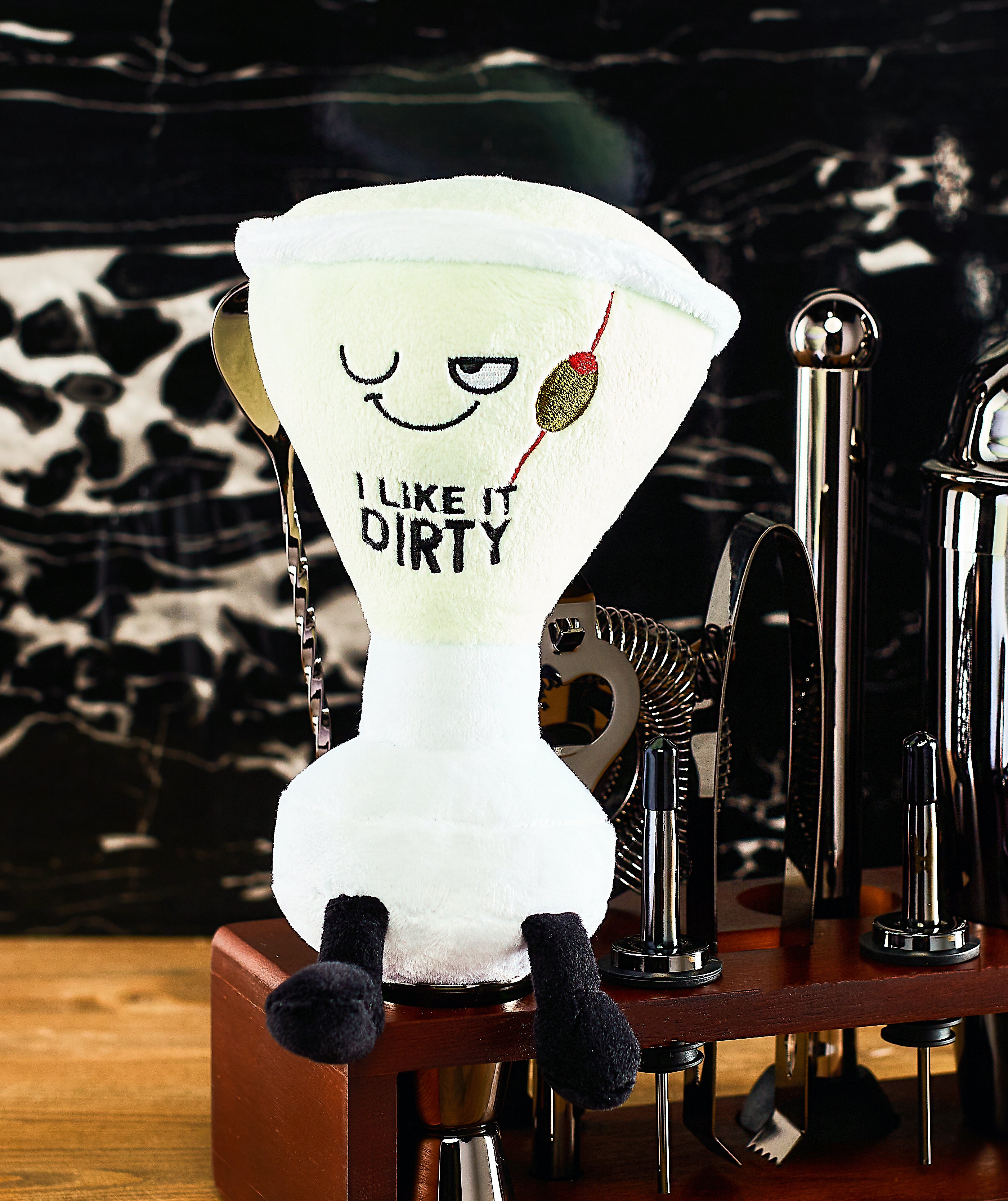 A plush resembling a martini glass with the phrase 'I LIKE IT DIRTY' embroidered on it on a bar cart.