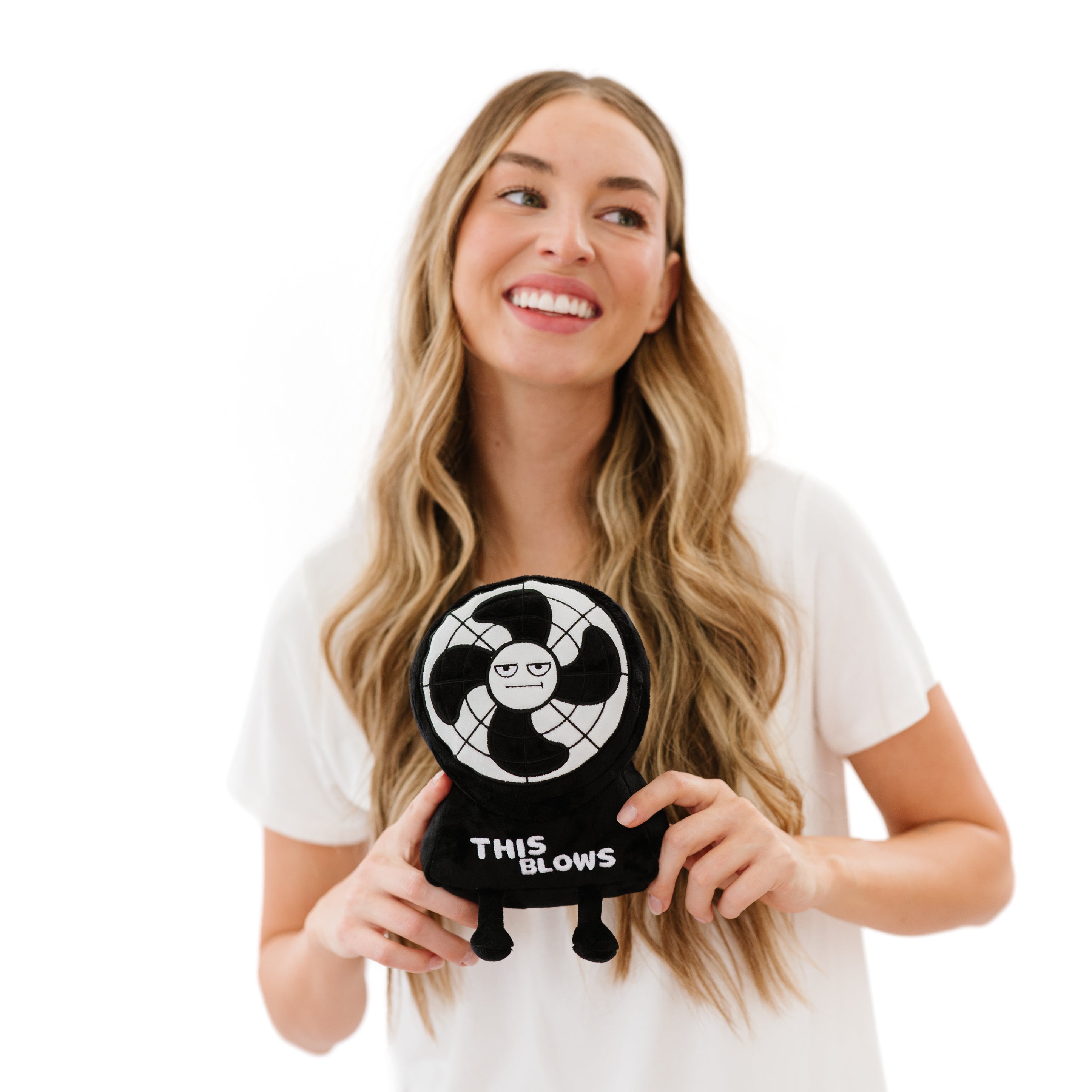 A model holding a plush in the shape of a fan with a grumpy expression and the text 'This Blows' on its base.