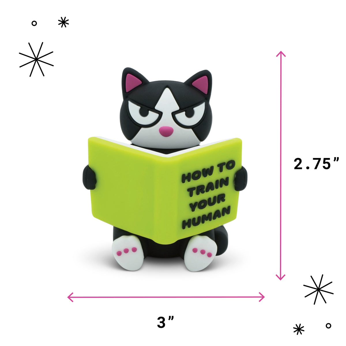 A small black-and-white cat figurine holding a bright yellow-green book that reads “HOW TO TRAIN YOUR HUMAN,” shown on a white background with pink dimension arrows and labels indicating 3 inches wide by 2.75 inches tall.