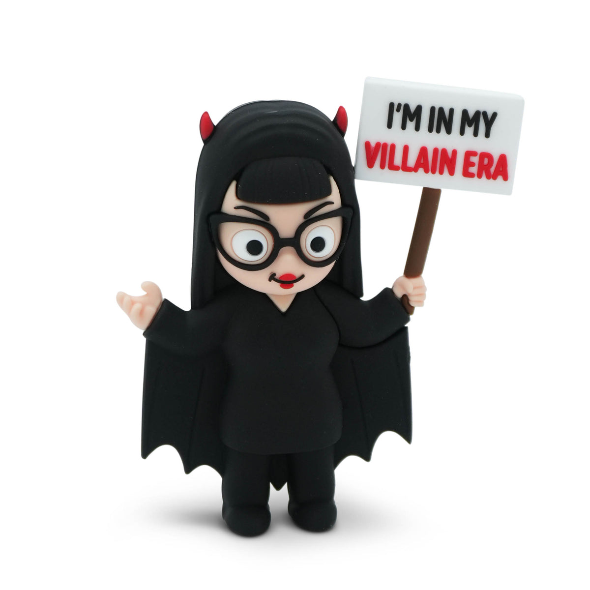 A plastic figure of a woman in a black costume with red devil horns, holding a sign that reads 'I'M IN MY VILLAIN ERA'. The figure is photographed on a clean white background.