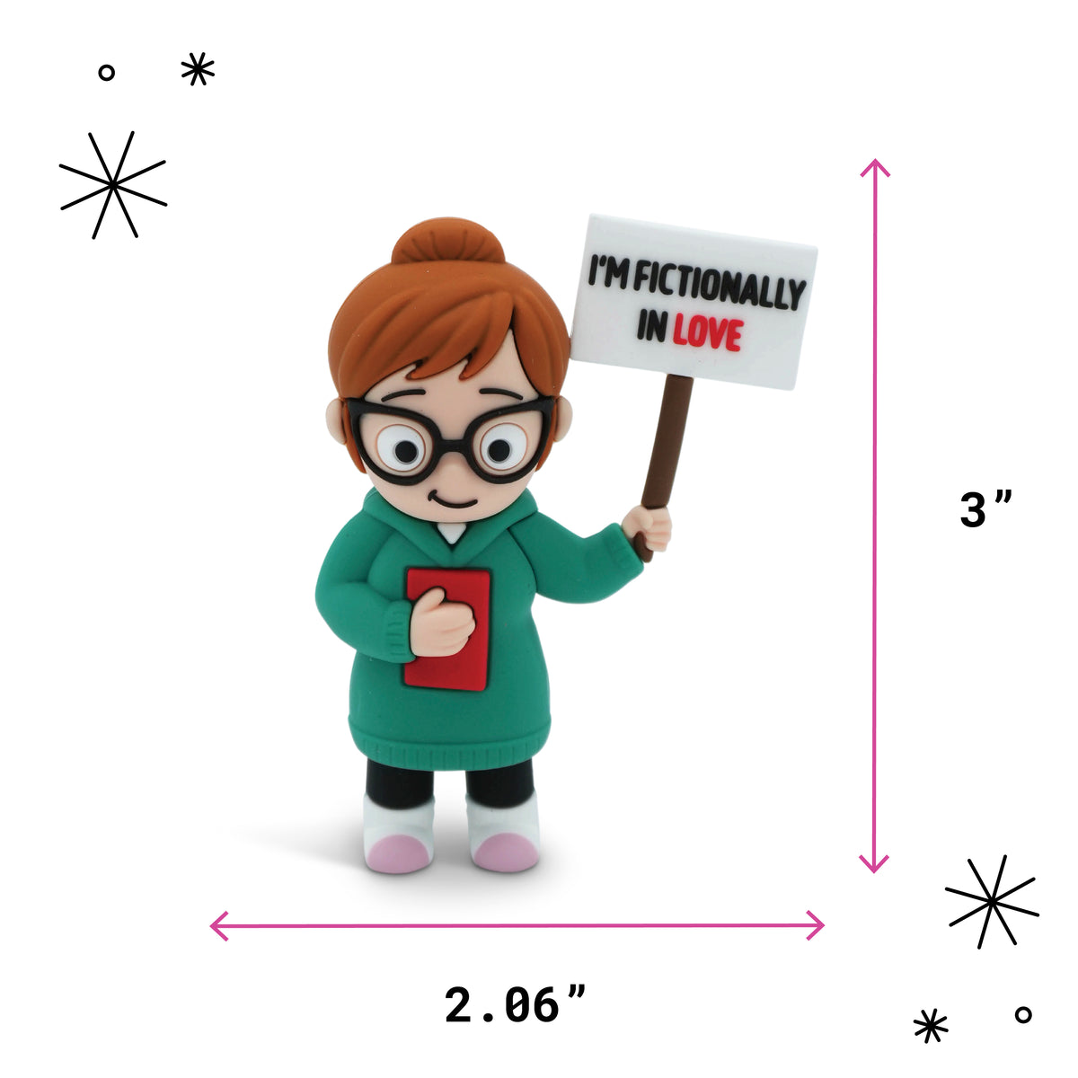 A small figurine of a woman with orange hair in a bun, wearing black glasses and a green coat, holding a sign that reads 'I'M FICTIONALLY IN LOVE' and a red book. Pink dimension arrows show the figurine is 3 inches tall.