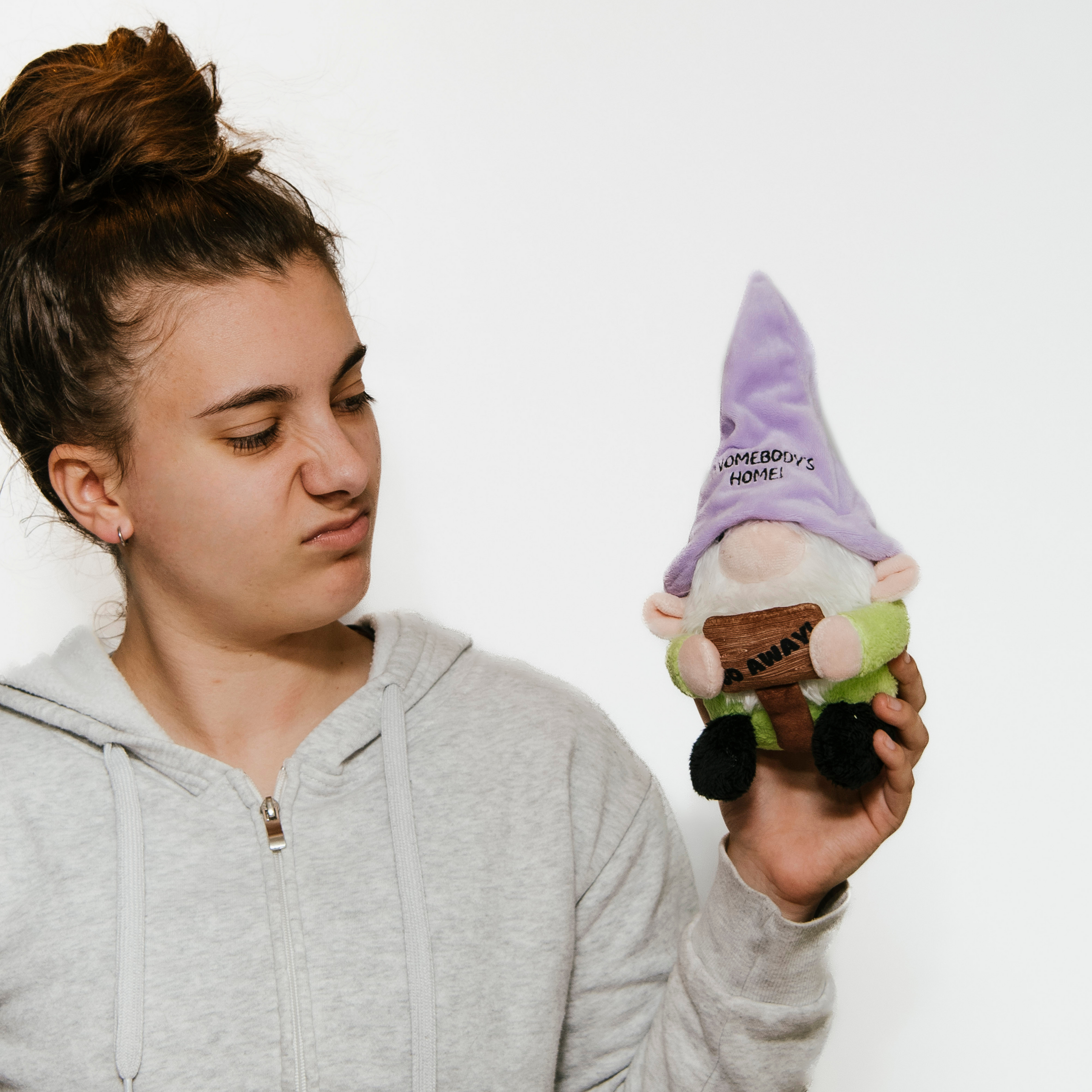 A model holding a plush gnome with a purple hat that says 'Gnomebody's Home' on it.