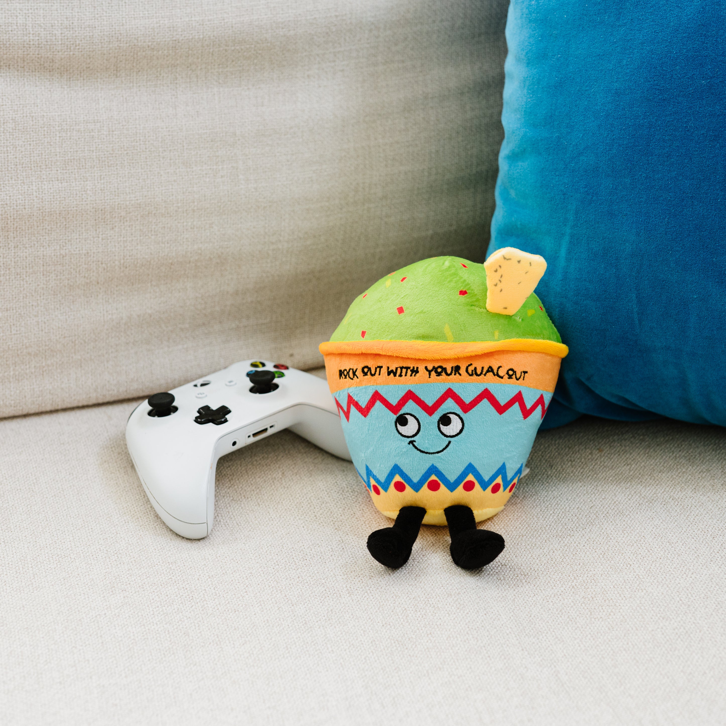 A guacamole bowl plush with the text 'ROCK OUT WITH YOUR GUAC OUT' placed on a couch.