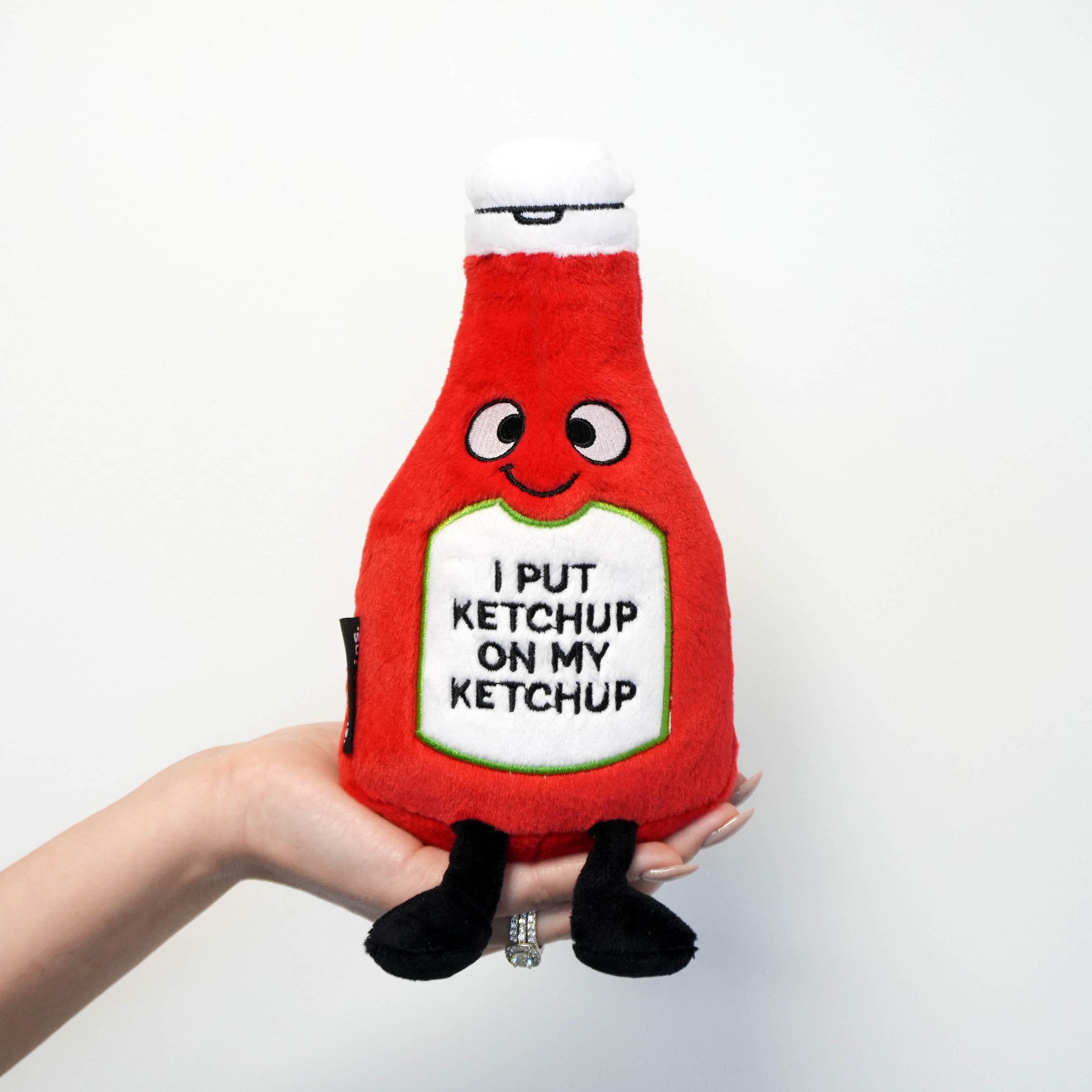 Hand holding plush toy resembling a ketchup on a white background