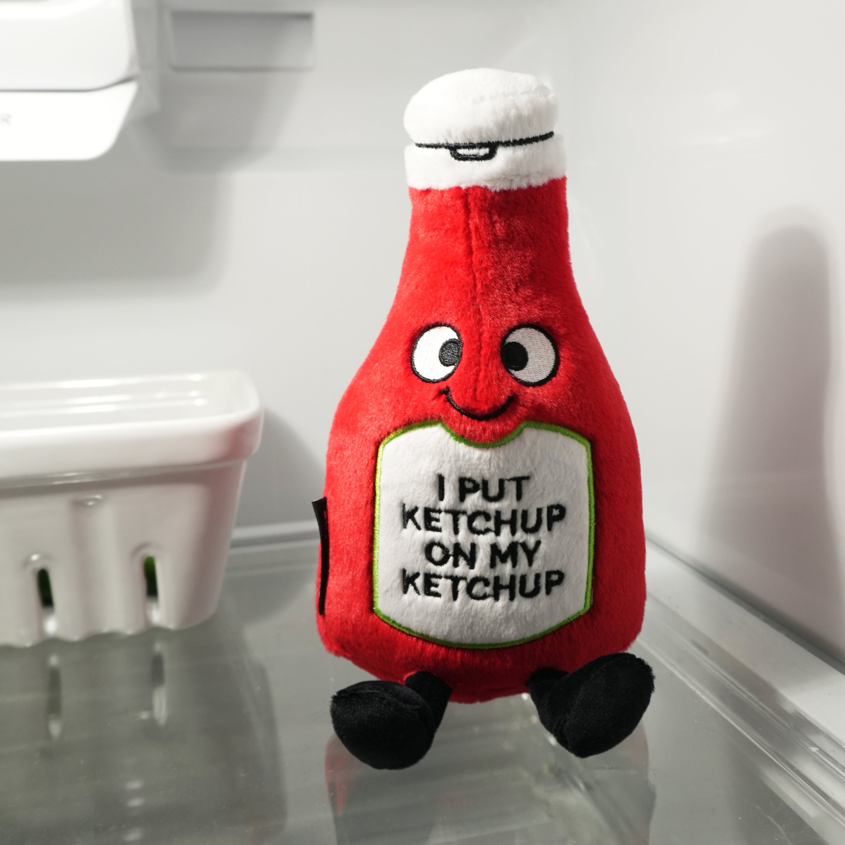 Plush toy shaped like a ketchup bottle with a humorous message inside of fridge.
