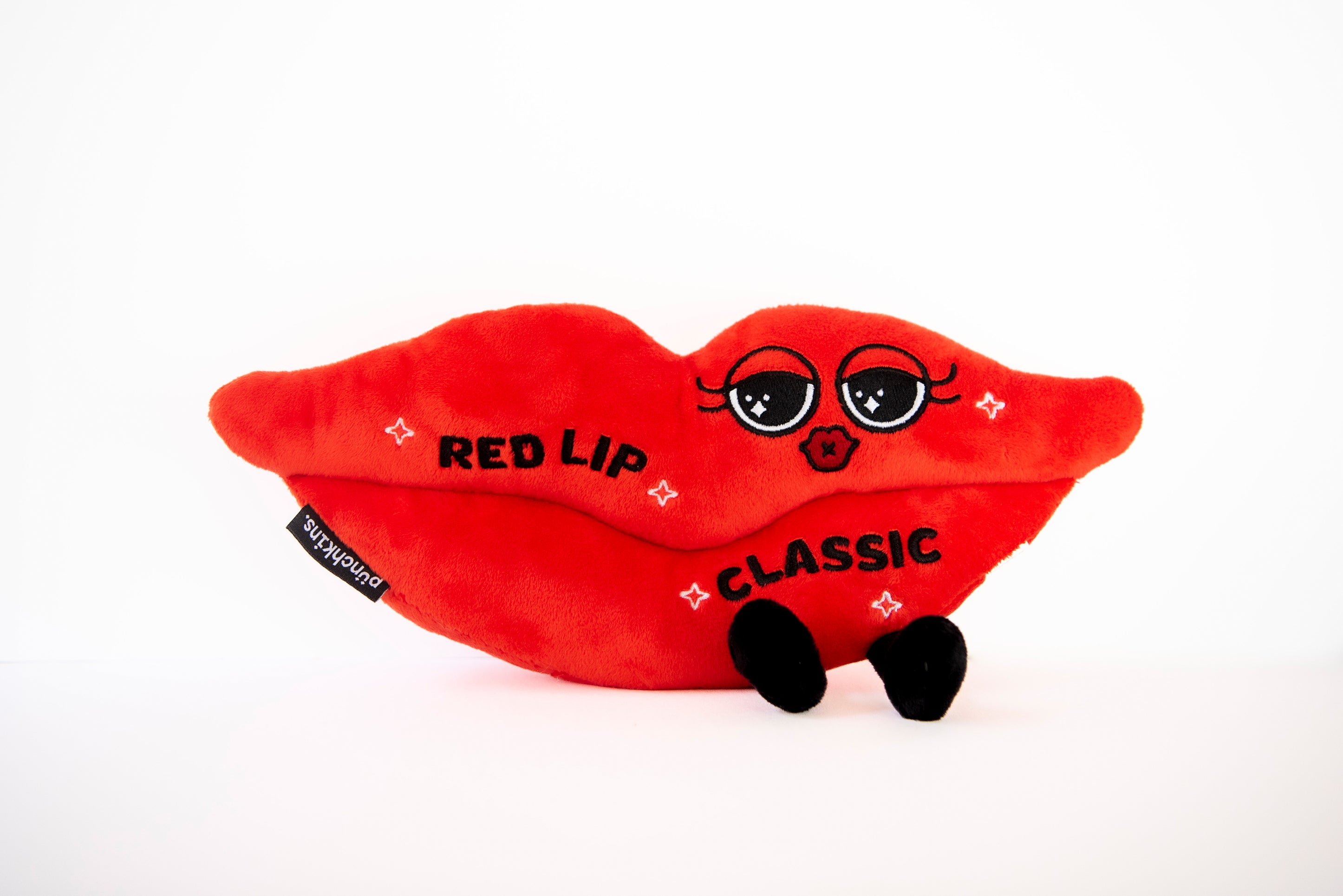 A plush designed to look like a red lip with "Red lip classic" written on it. It also has eyes and legs on a white background.