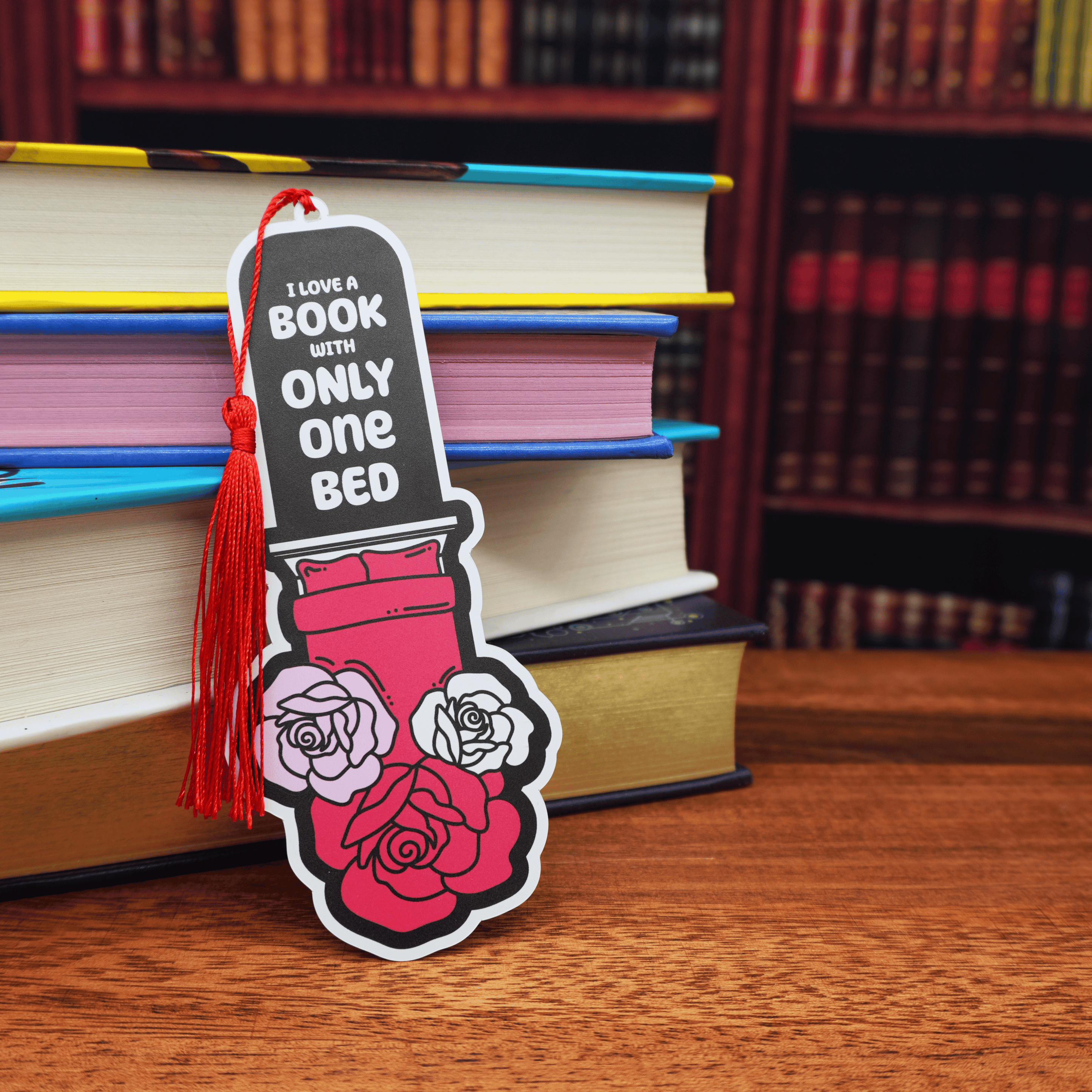 Bookmark with roses and a bed with the text 'I love a book with only one bed' on a wooden surface with books in the background.