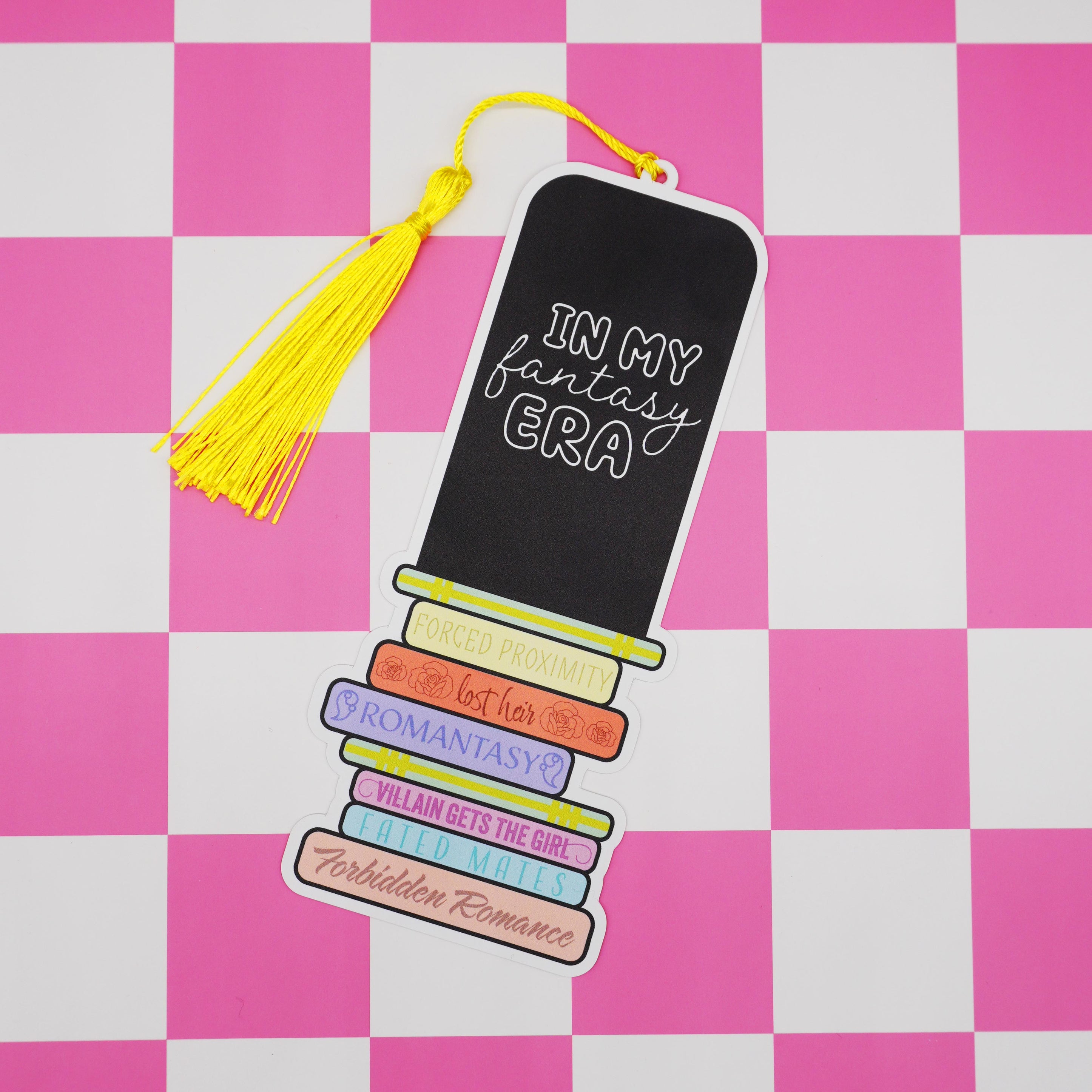 Bookmark with romantasy tropes and a tassel on a pink and white checkered background