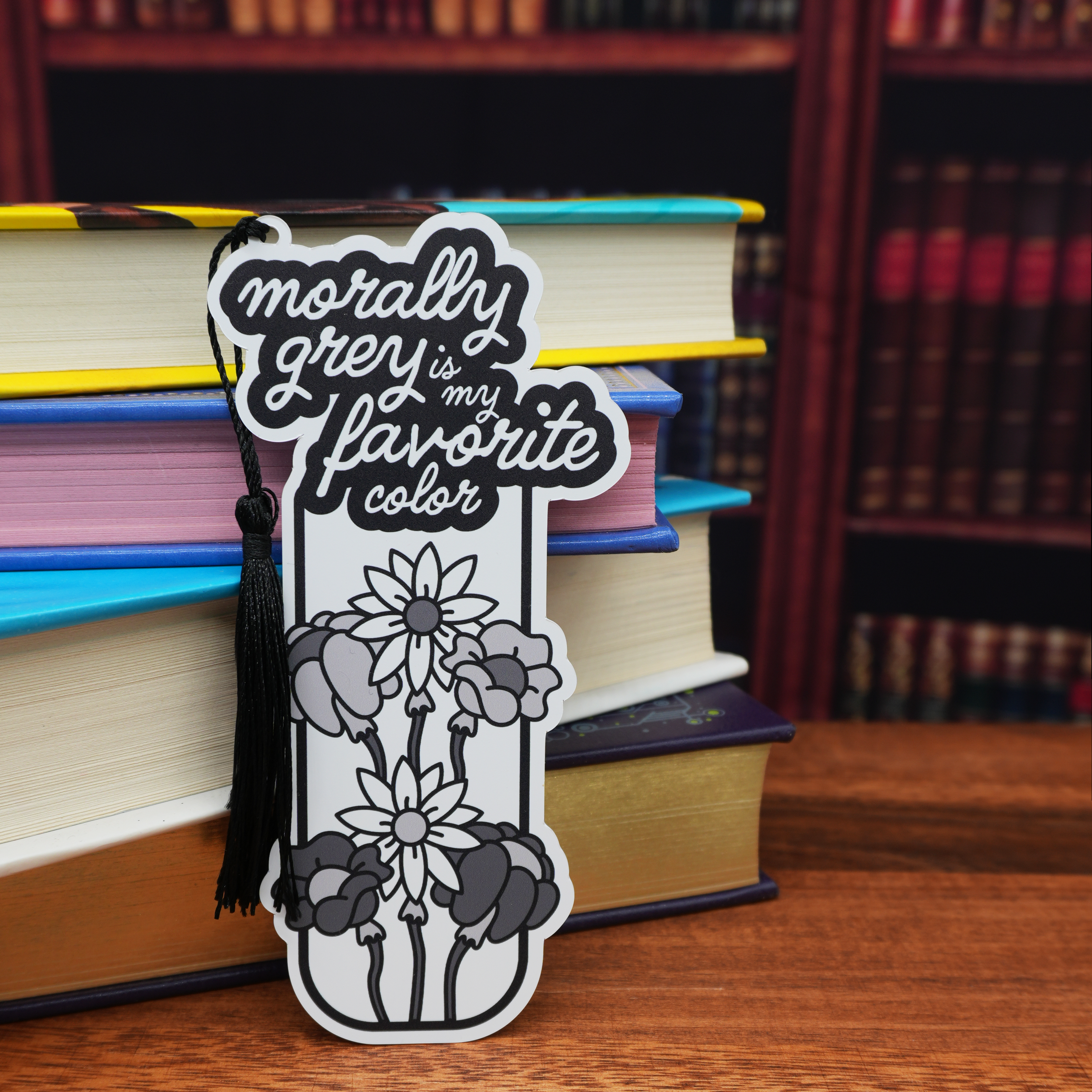 Bookmark with floral design and text 'morally grey is my favorite color' on a stack of books.