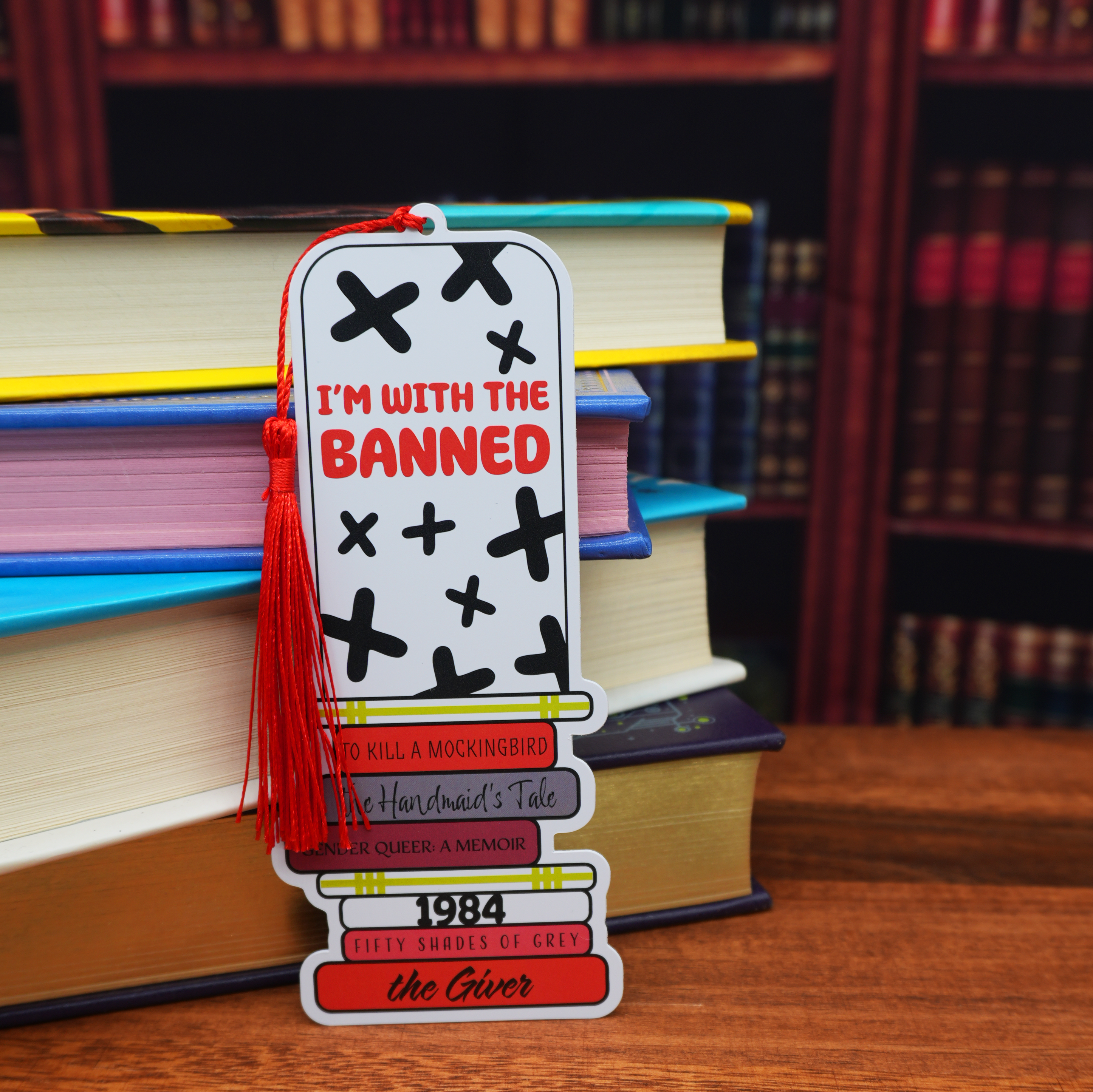 Bookmark with text and tassel on a stack of books with a blurred bookshelf background