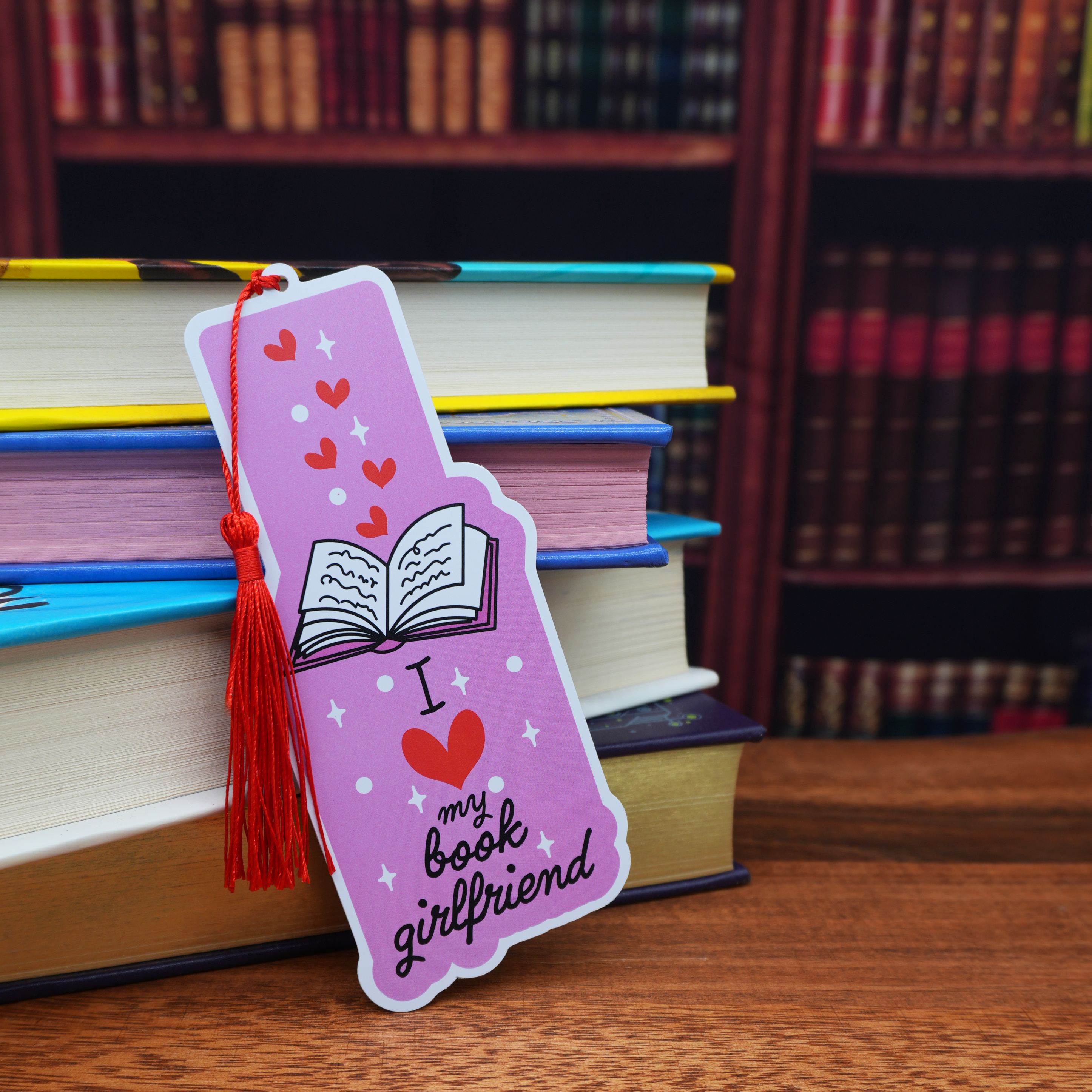Pink bookmark with tassel and 'I love my book girlfriend' text on a stack of books.