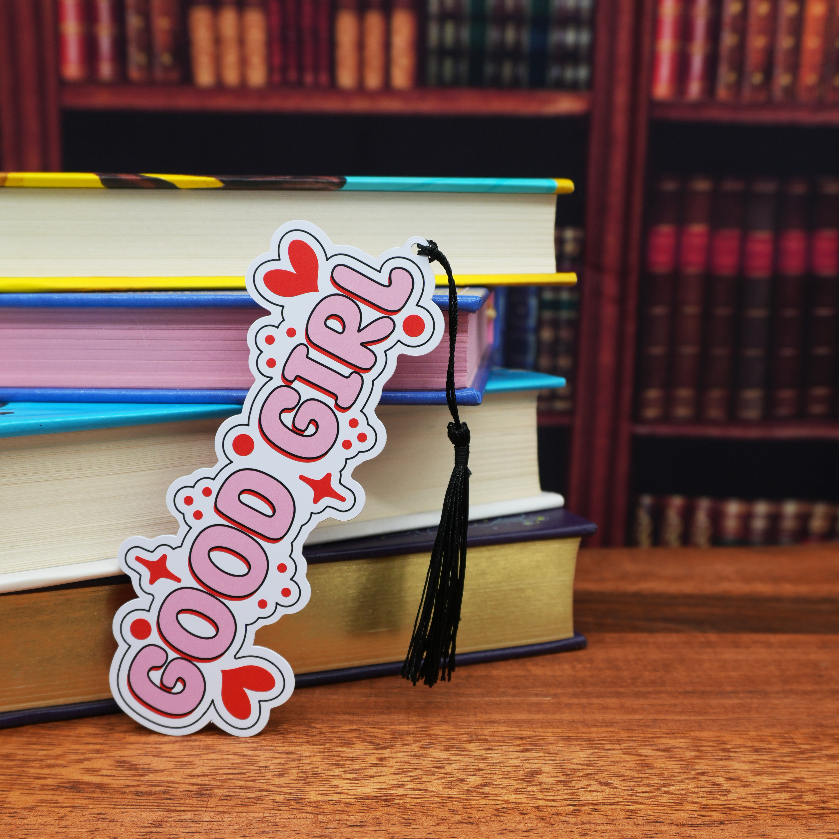 Bookmark with 'Good Girl' design on a stack of books in a library setting
