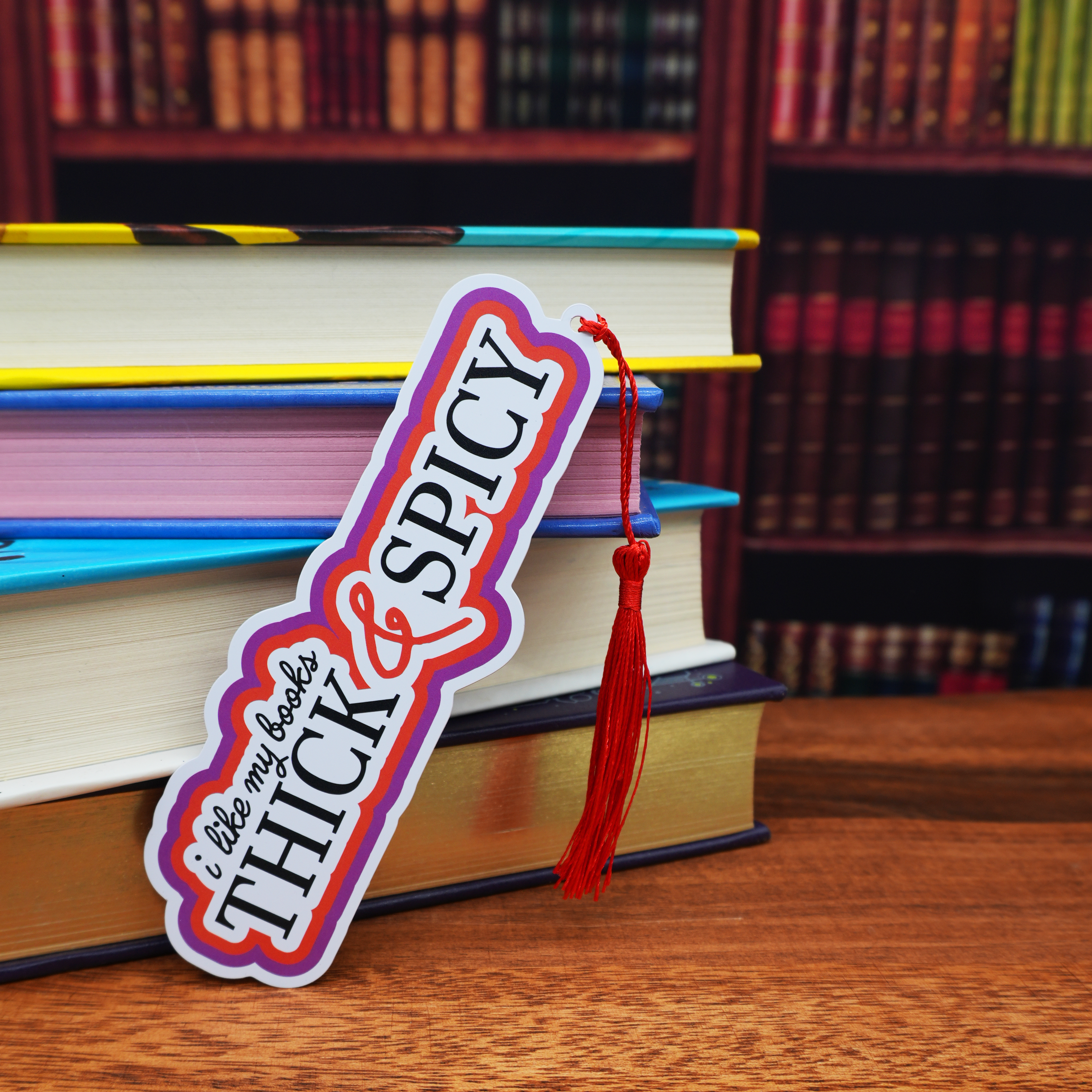 Bookmark with 'Thick & Spicy' text and tassel on books with a bookshelf background
