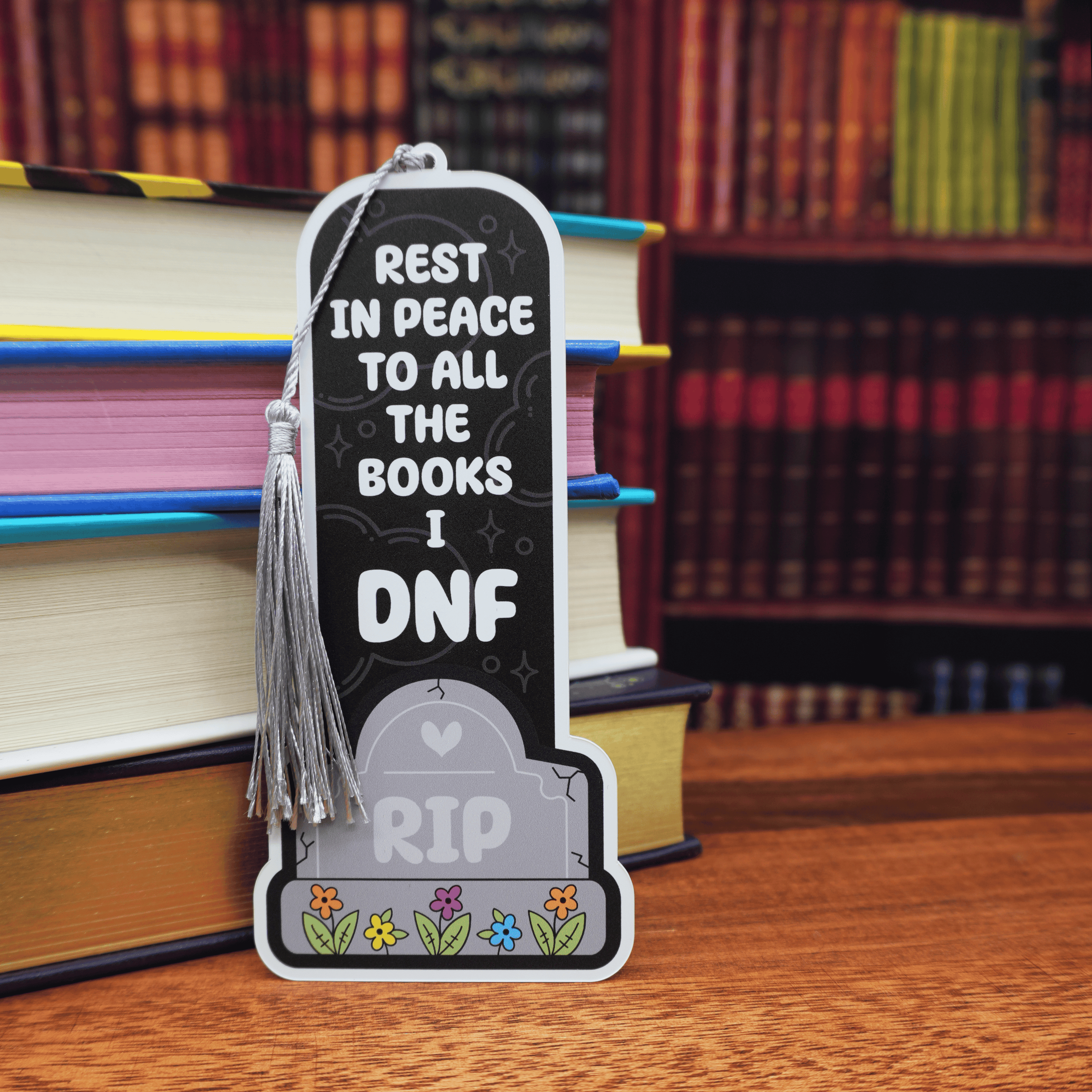 Bookmark with 'Rest in Peace to all the books I DNF' text on a wooden surface with books in the background