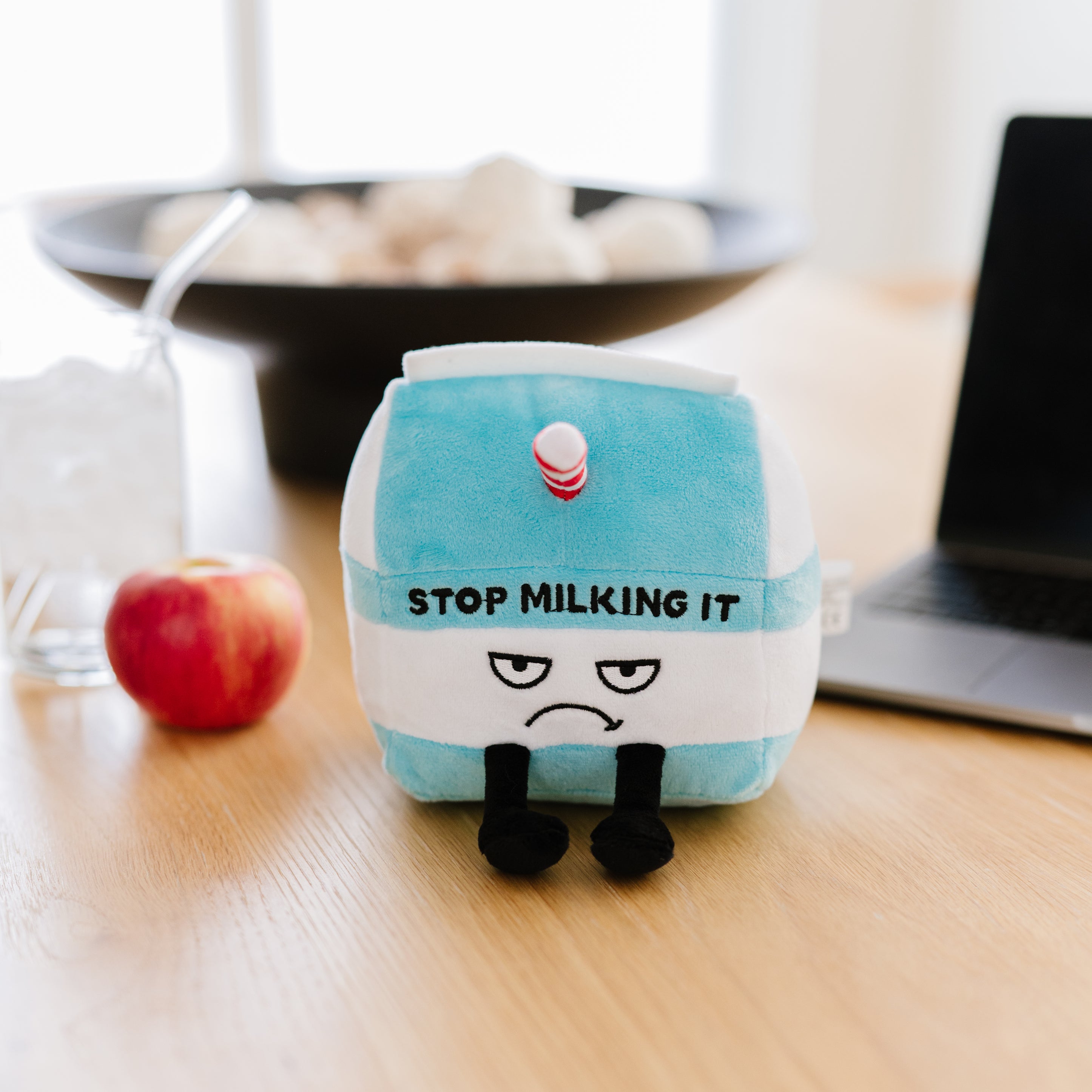 A plush designed to resemble a milk carton with the text 'Stop Milking It' placed on a kitchen table. 